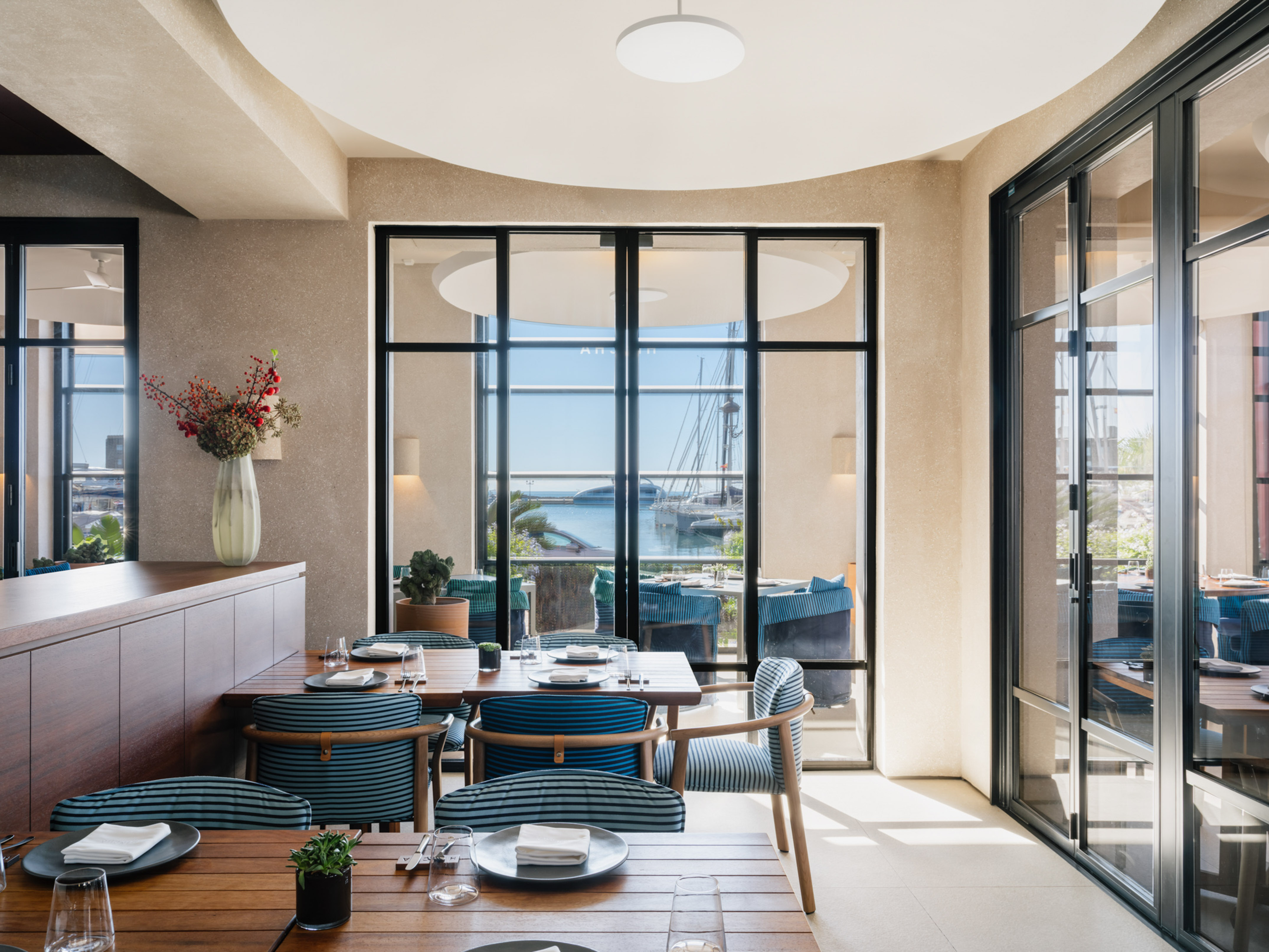 Modern restaurant dining room with marina view, wooden tables, and blue chairs.