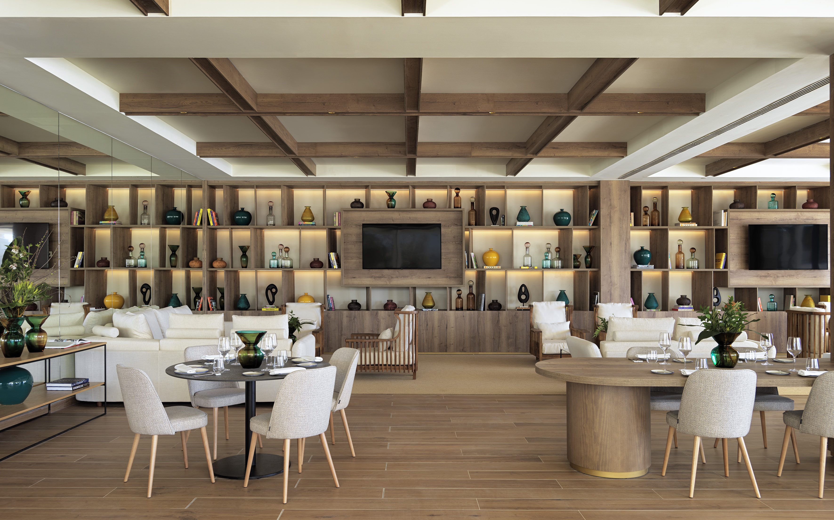Contemporary lounge interior with wooden shelving, colorful vases, and seating areas.