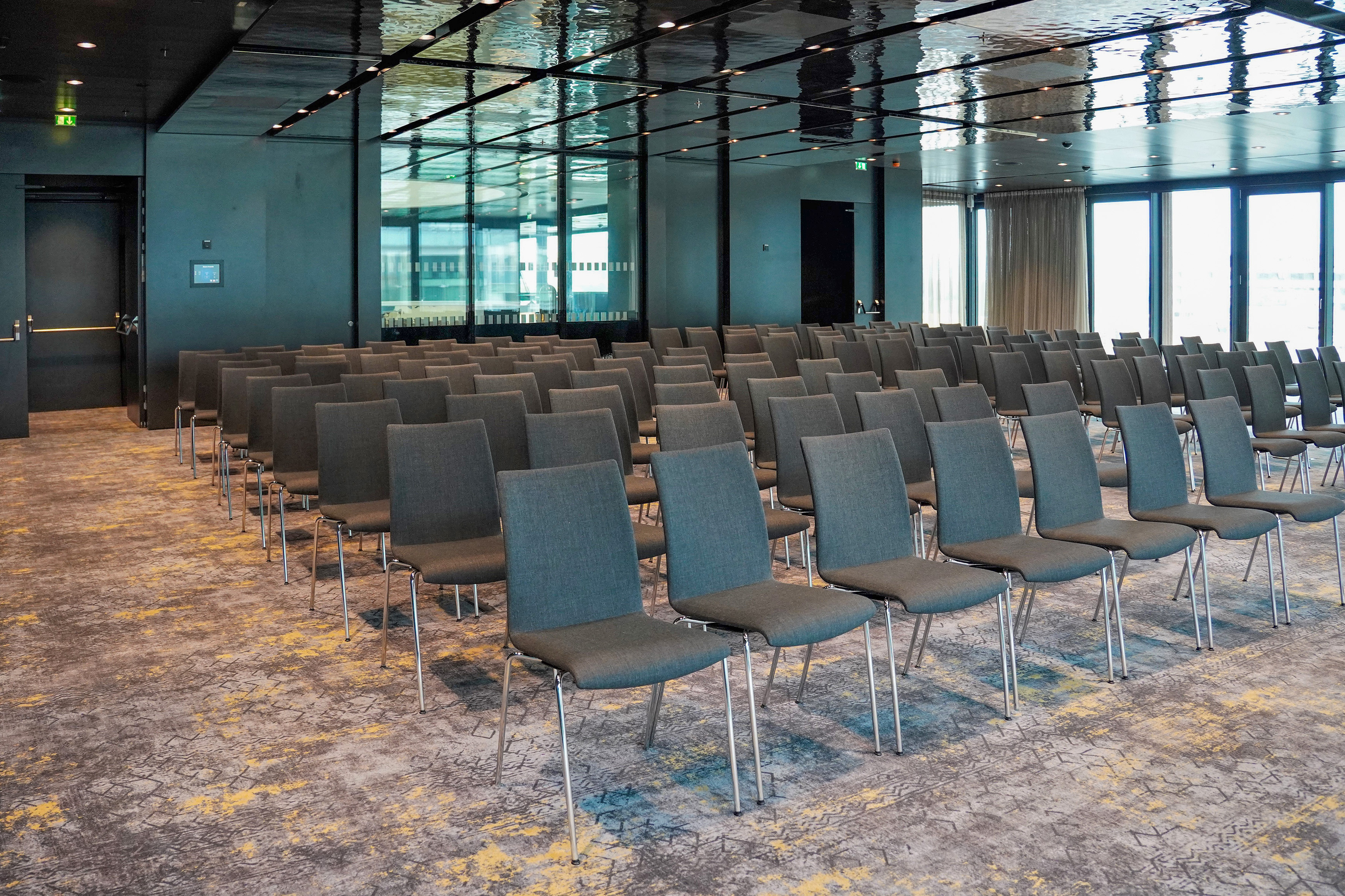 Modern empty conference room with rows of gray chairs and large windows.