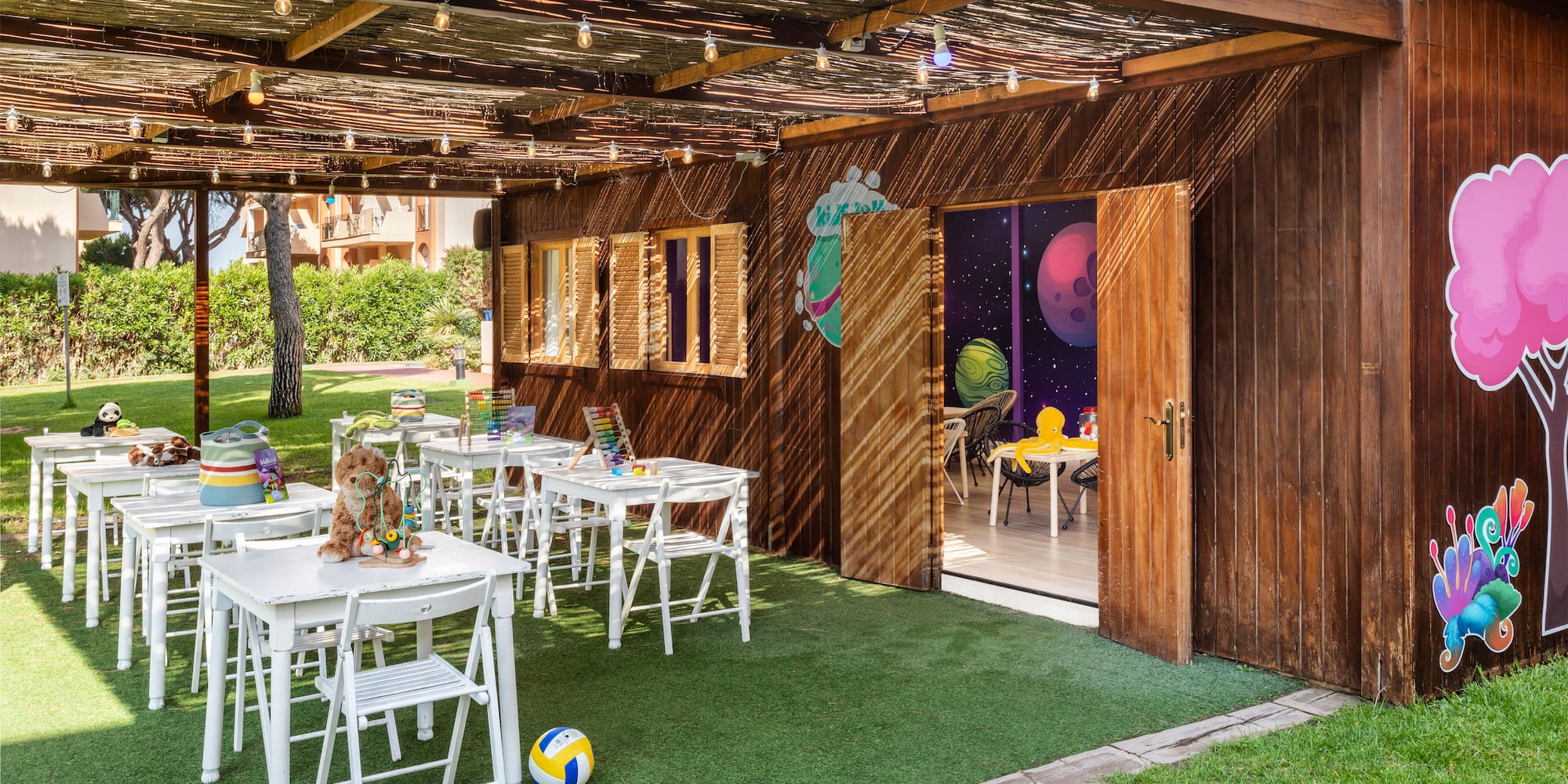 Outdoor kids' club with white tables, toys, and space-themed playhouse.