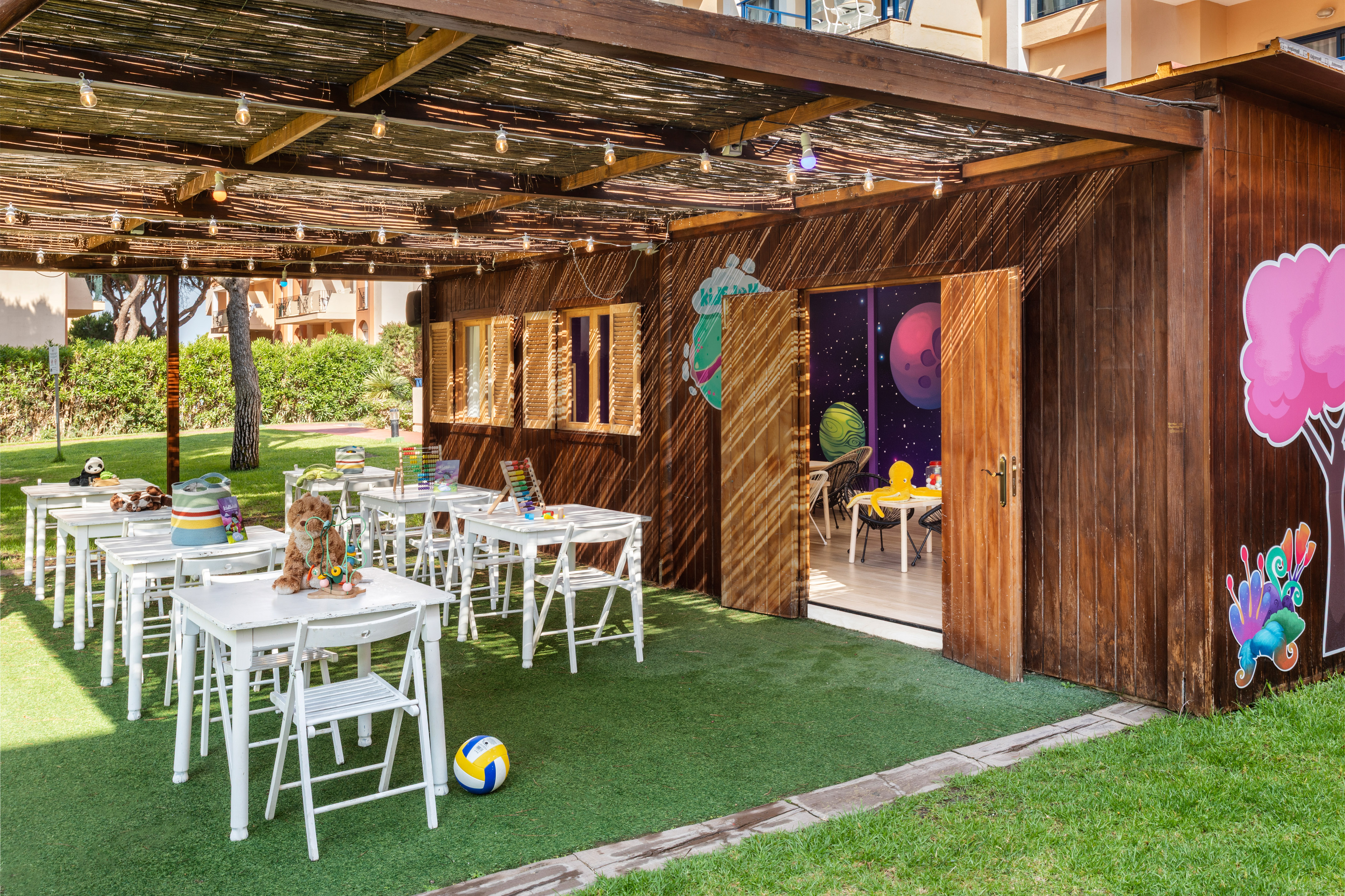 Outdoor kids' club with white tables, toys, and space-themed playhouse.