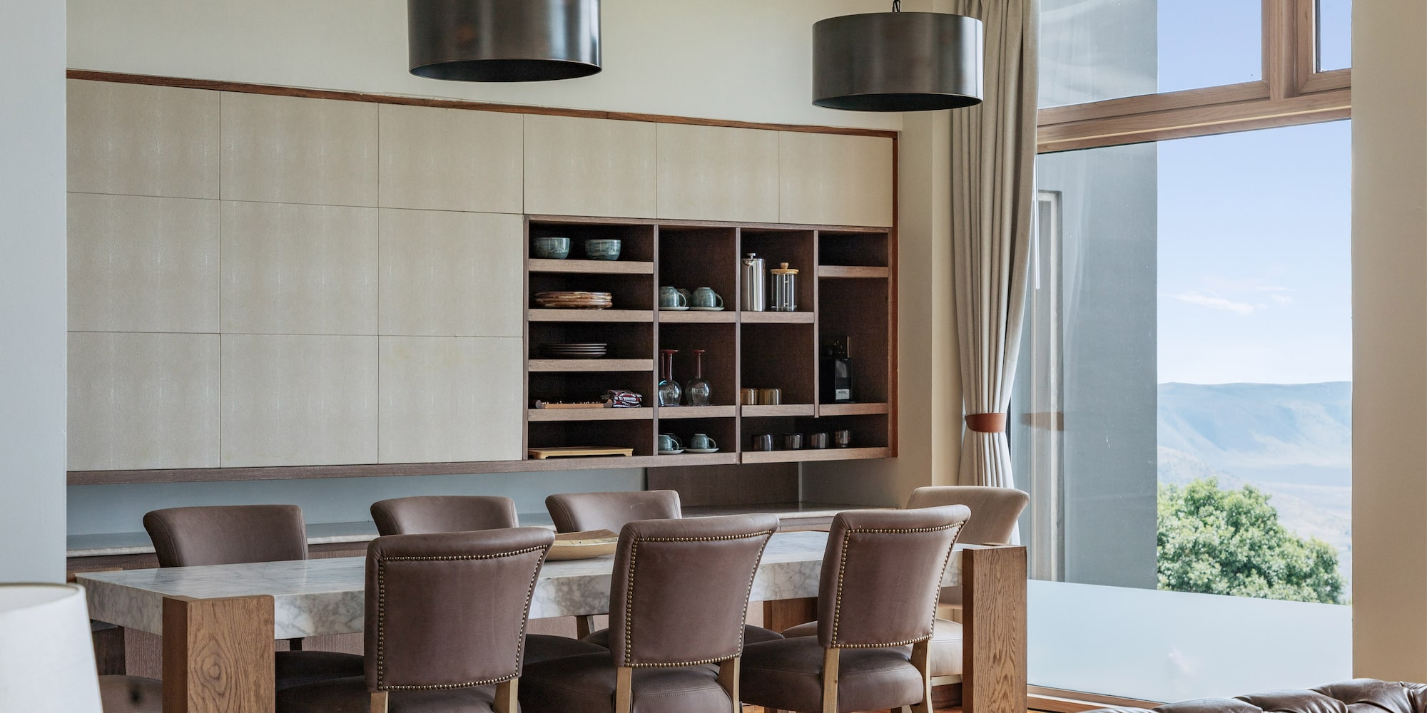 Modern dining area: marble table, leather chairs, built-in cabinet, mountain view.