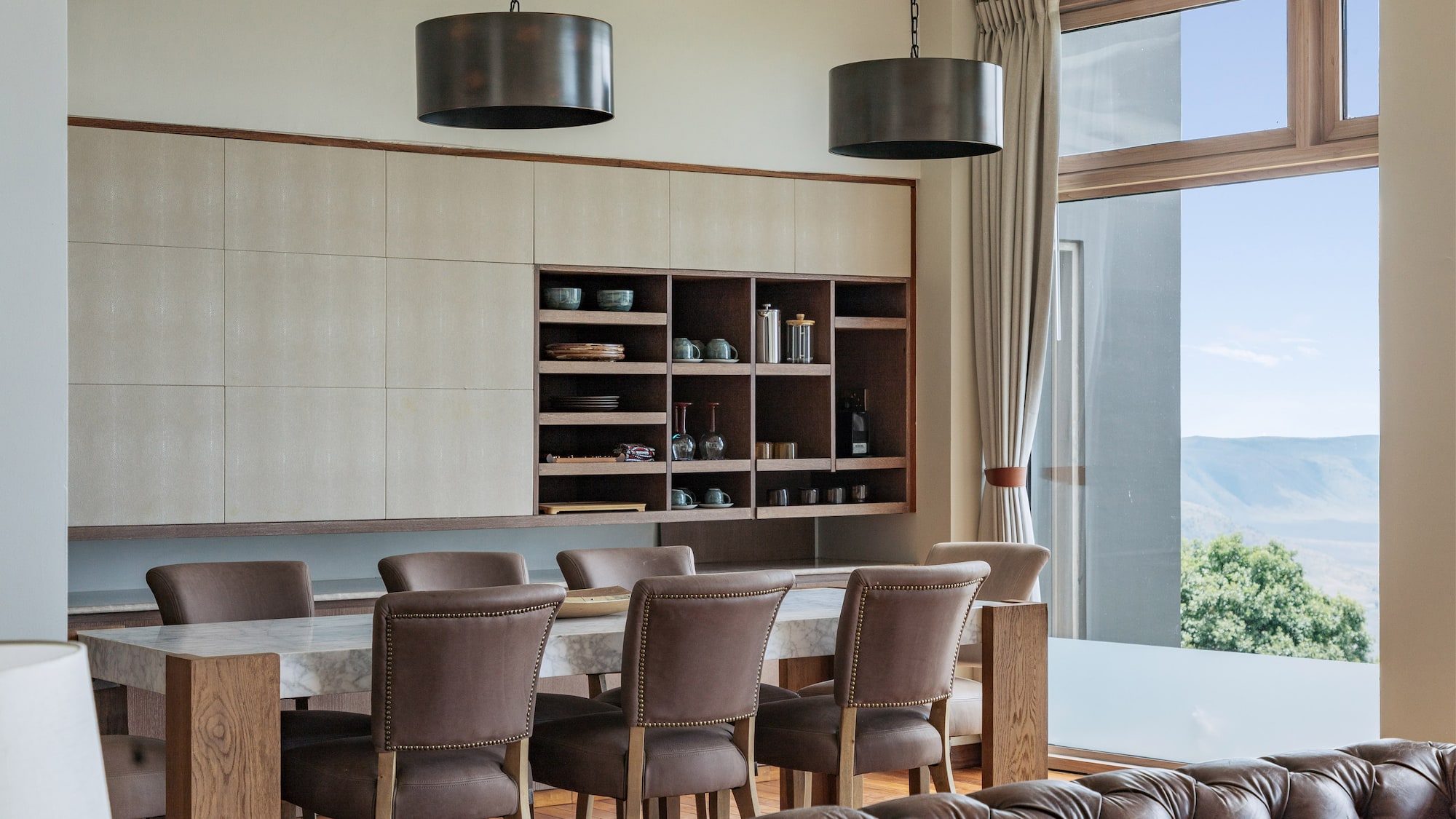 Modern dining area: marble table, leather chairs, built-in cabinet, mountain view.