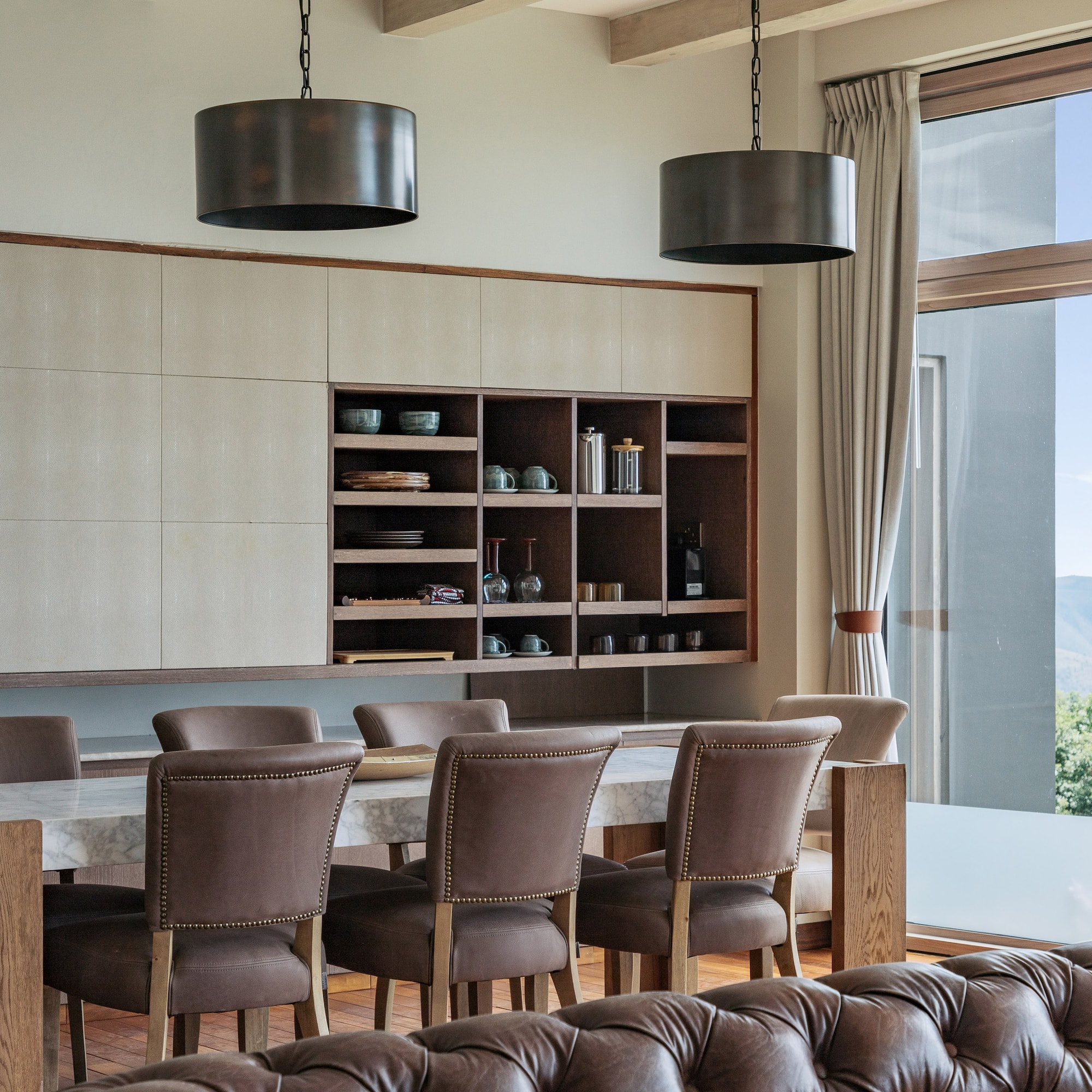 Modern dining area: marble table, leather chairs, built-in cabinet, mountain view.
