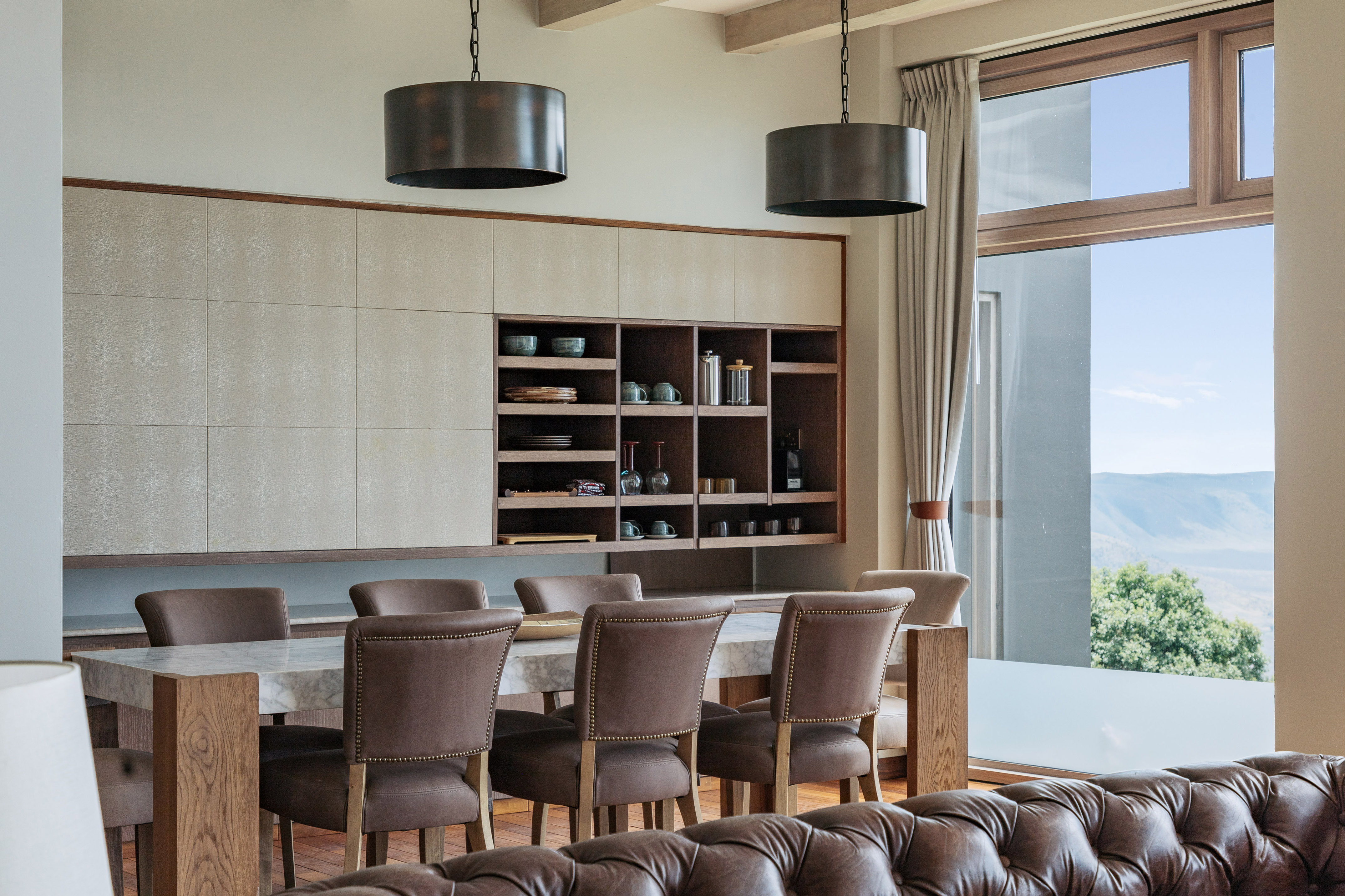 Modern dining area: marble table, leather chairs, built-in cabinet, mountain view.
