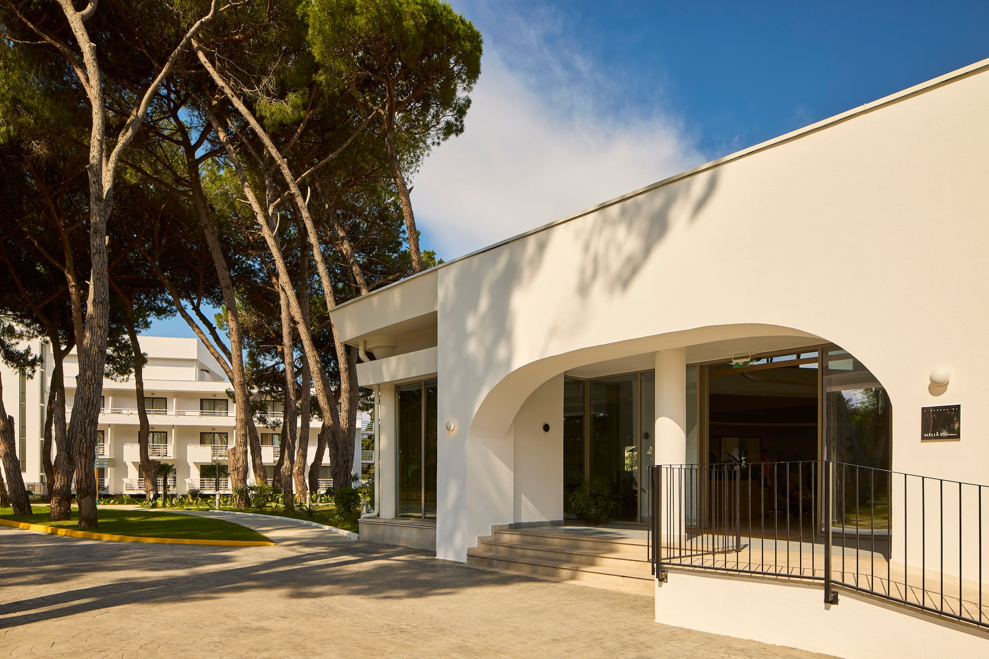 White modern hotel entrance with arched doorway and tall pine trees.