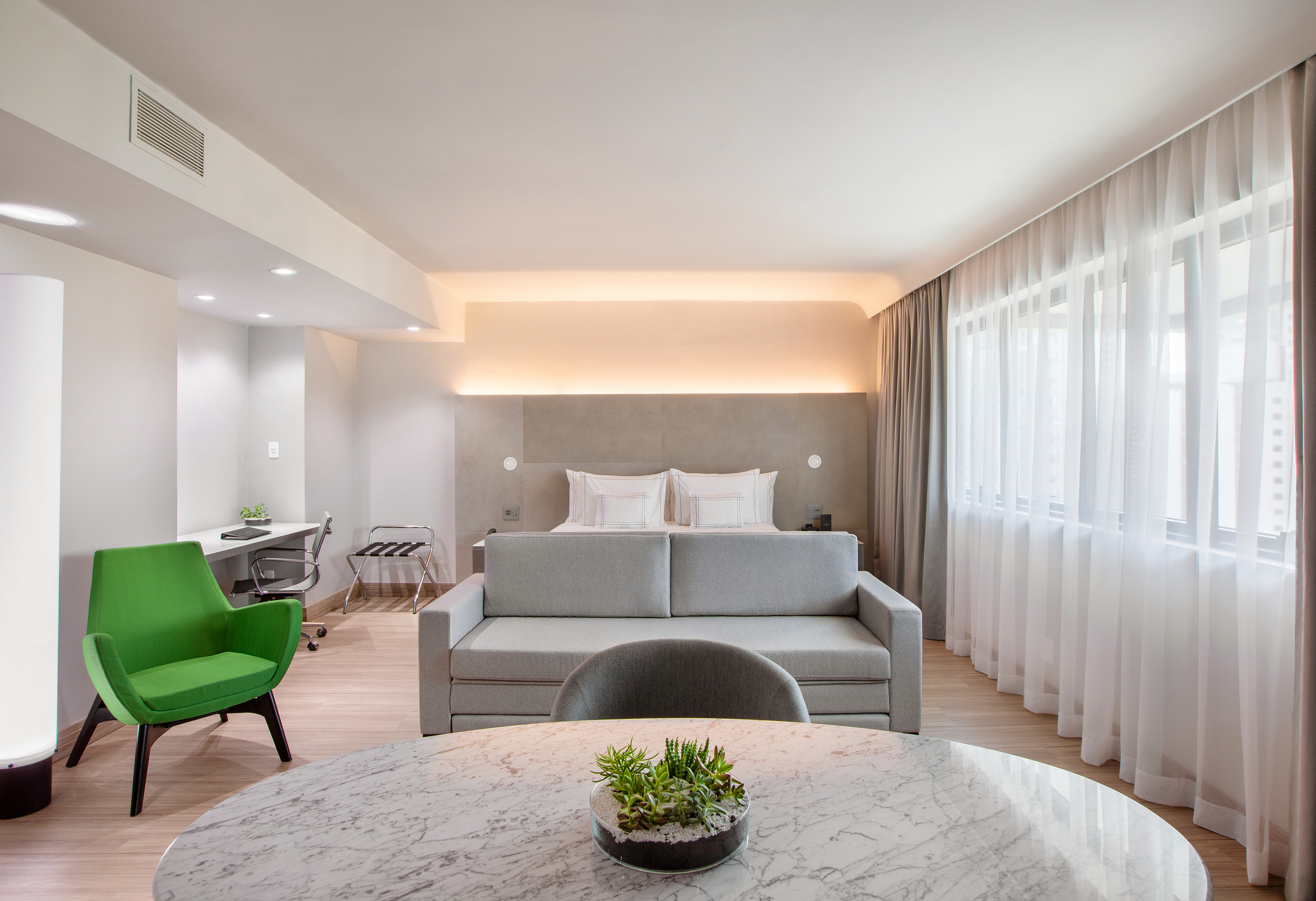Contemporary hotel suite with bed, sofa bed, desk, and chic green armchair.