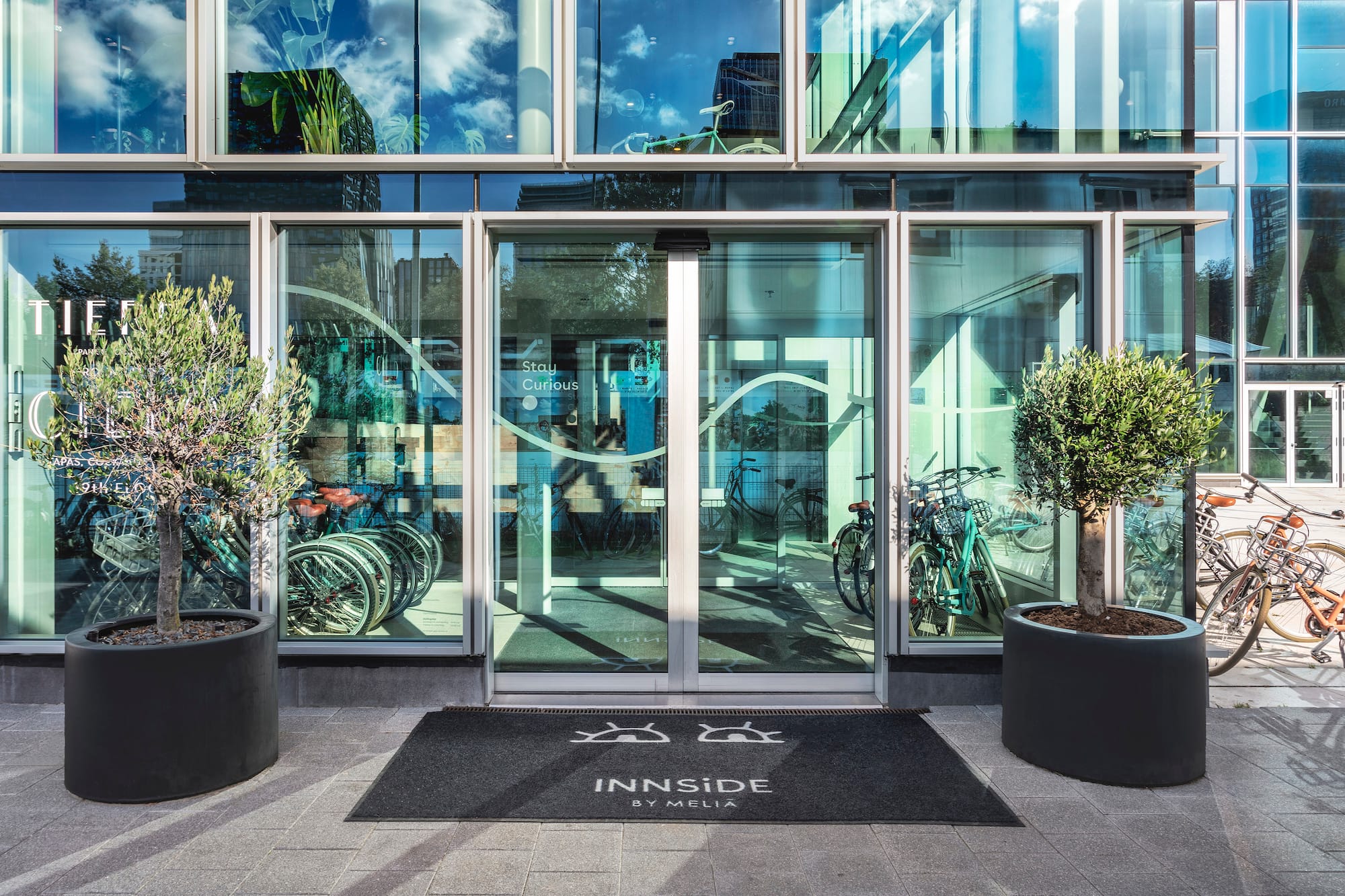 INNSIDE BY MELIA hotel entrance, glass facade, olive trees, bicycles.