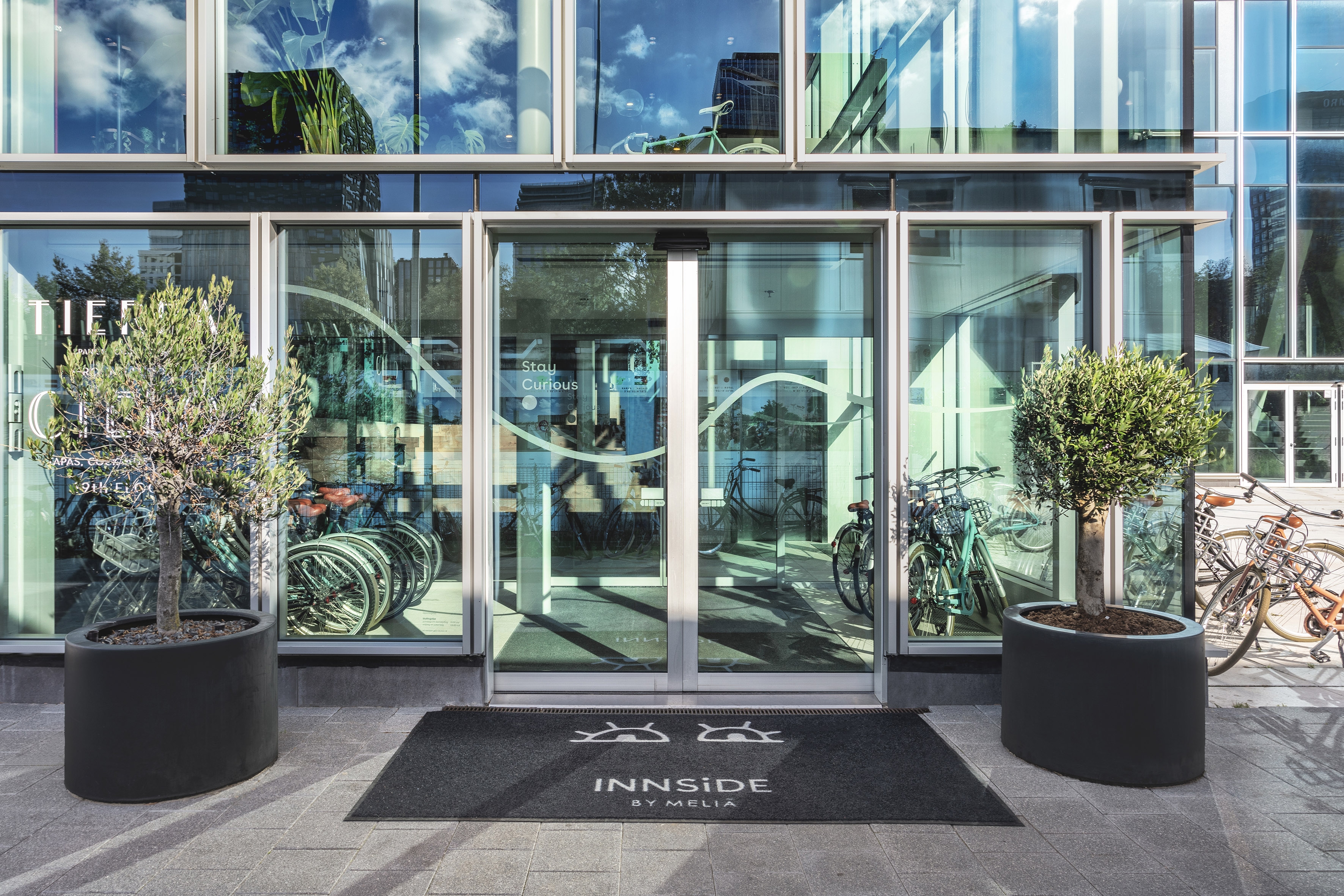 INNSIDE BY MELIA hotel entrance, glass facade, olive trees, bicycles.