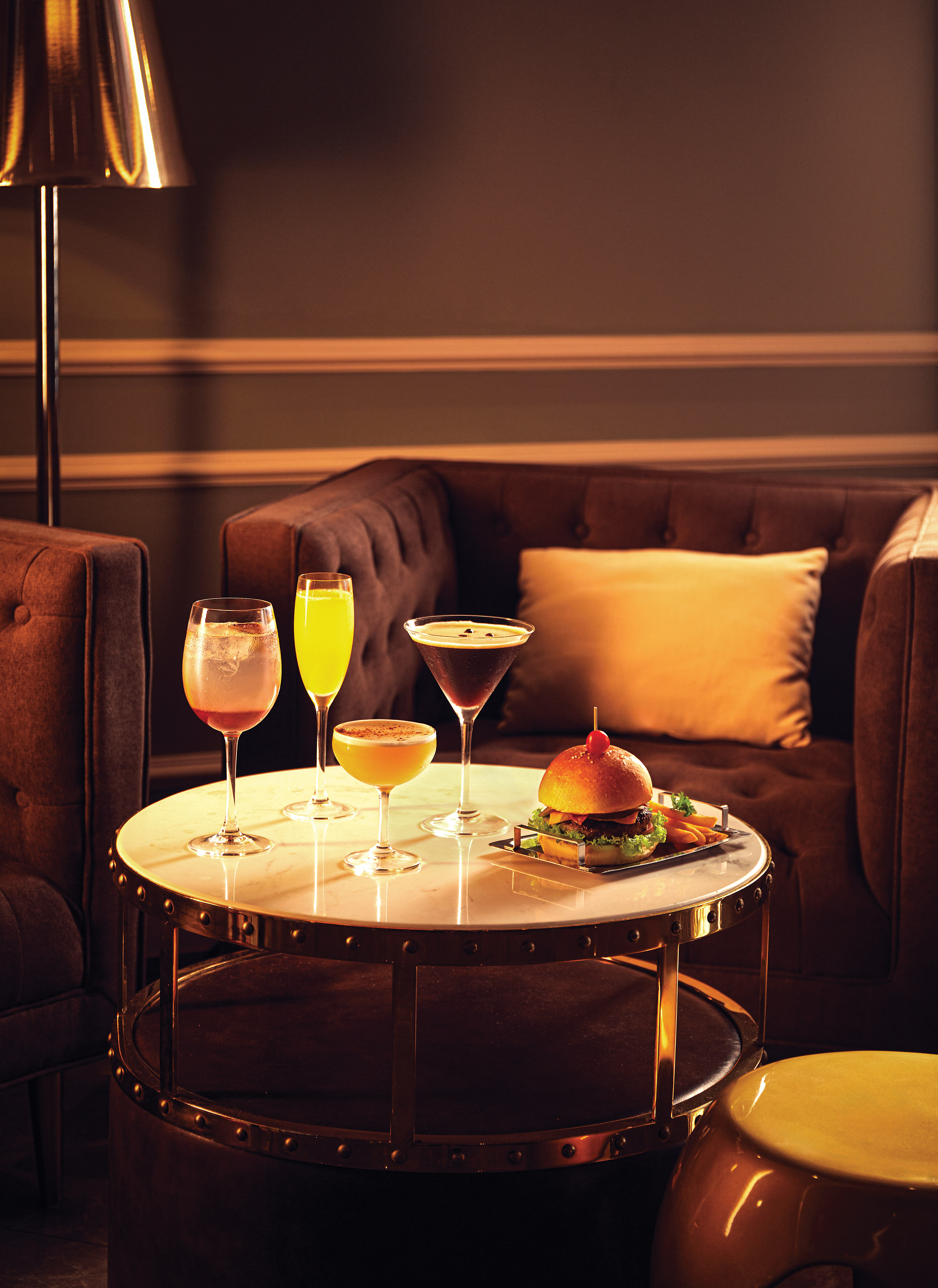 Gourmet burger, fries, and colorful cocktails on a marble lounge table.