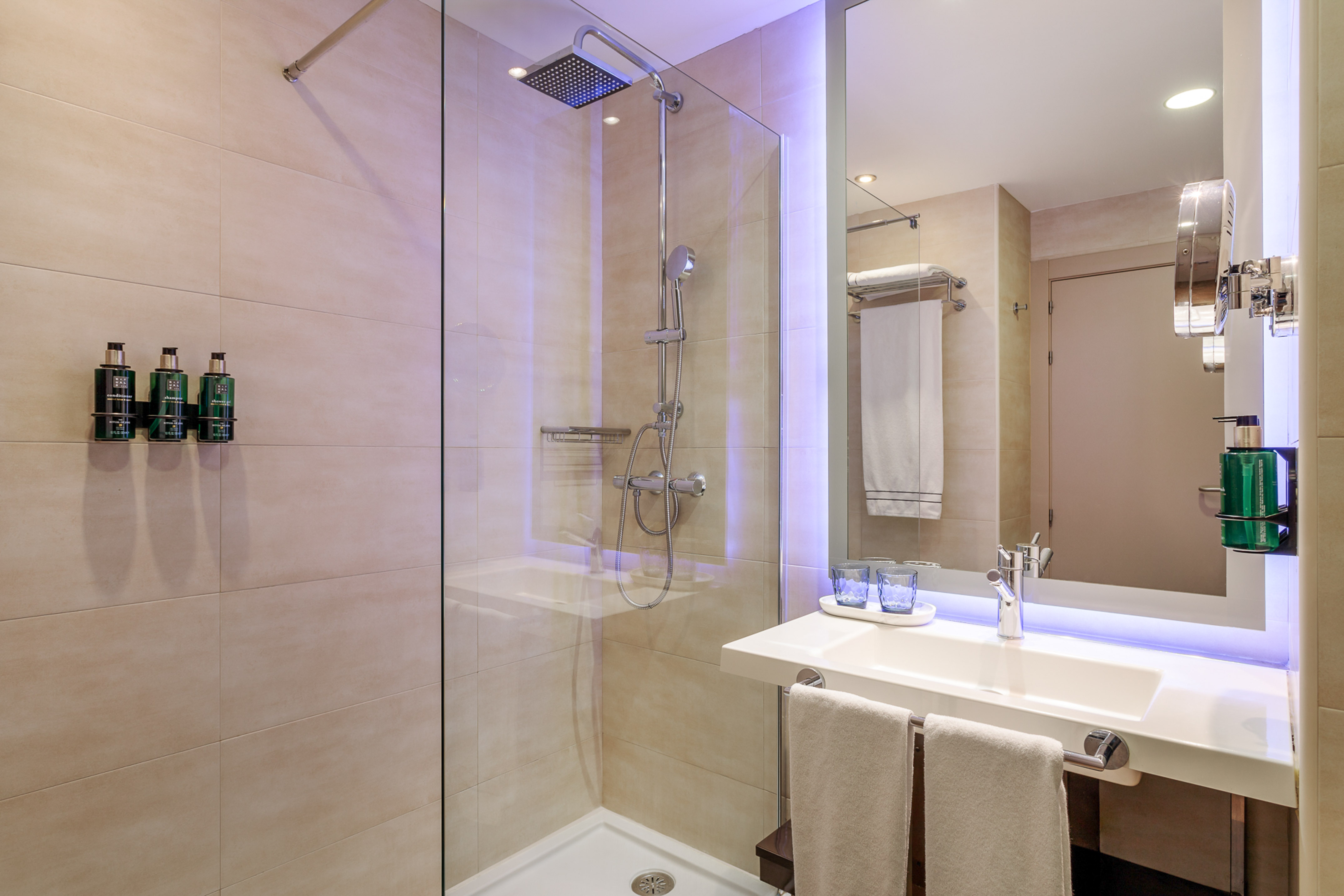 Modern bathroom with glass shower, rain shower, backlit mirror, and sink.