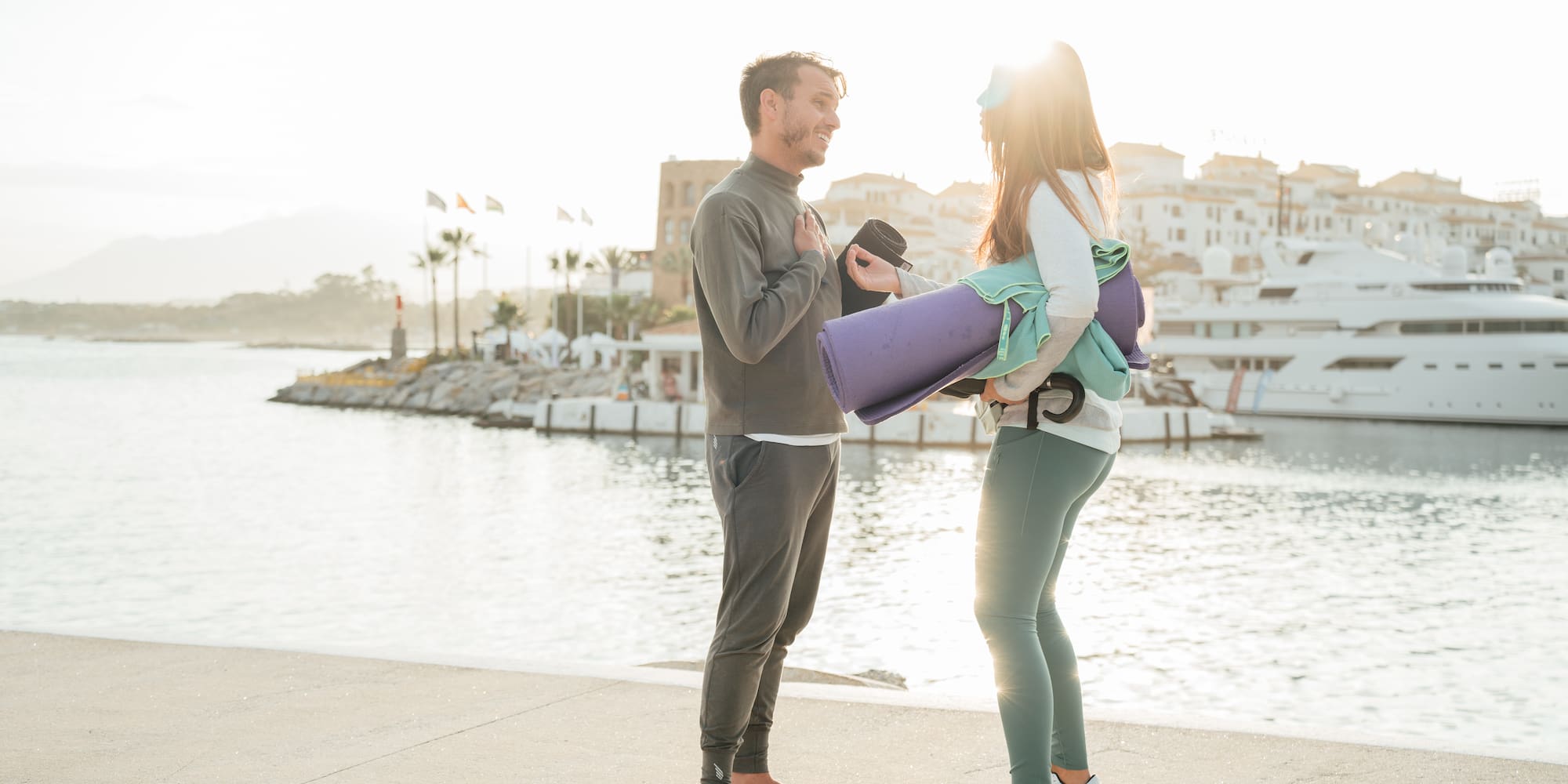 a man and woman standing on a dock with water and buildings in the background