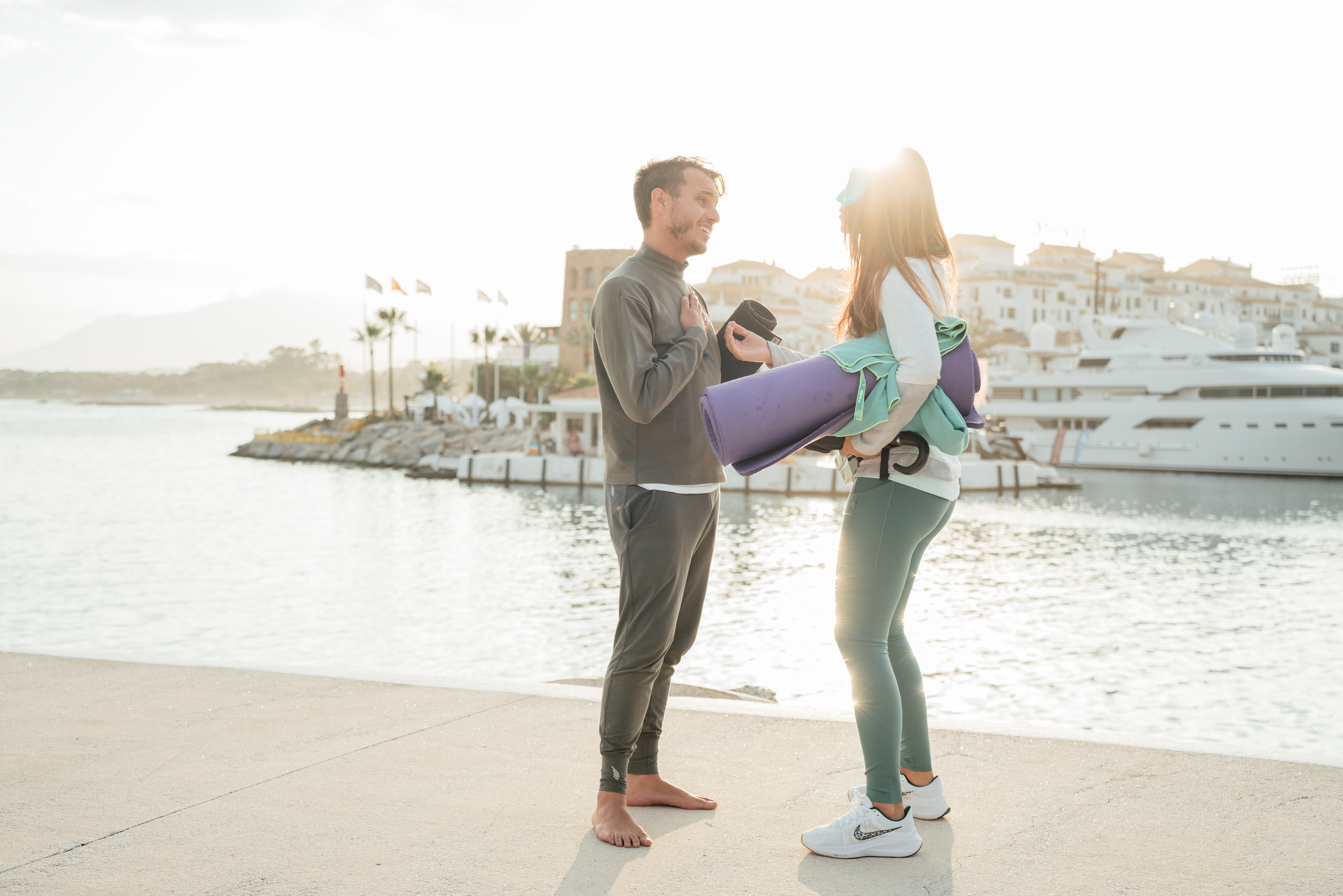 a man and woman standing on a dock with water and buildings in the background