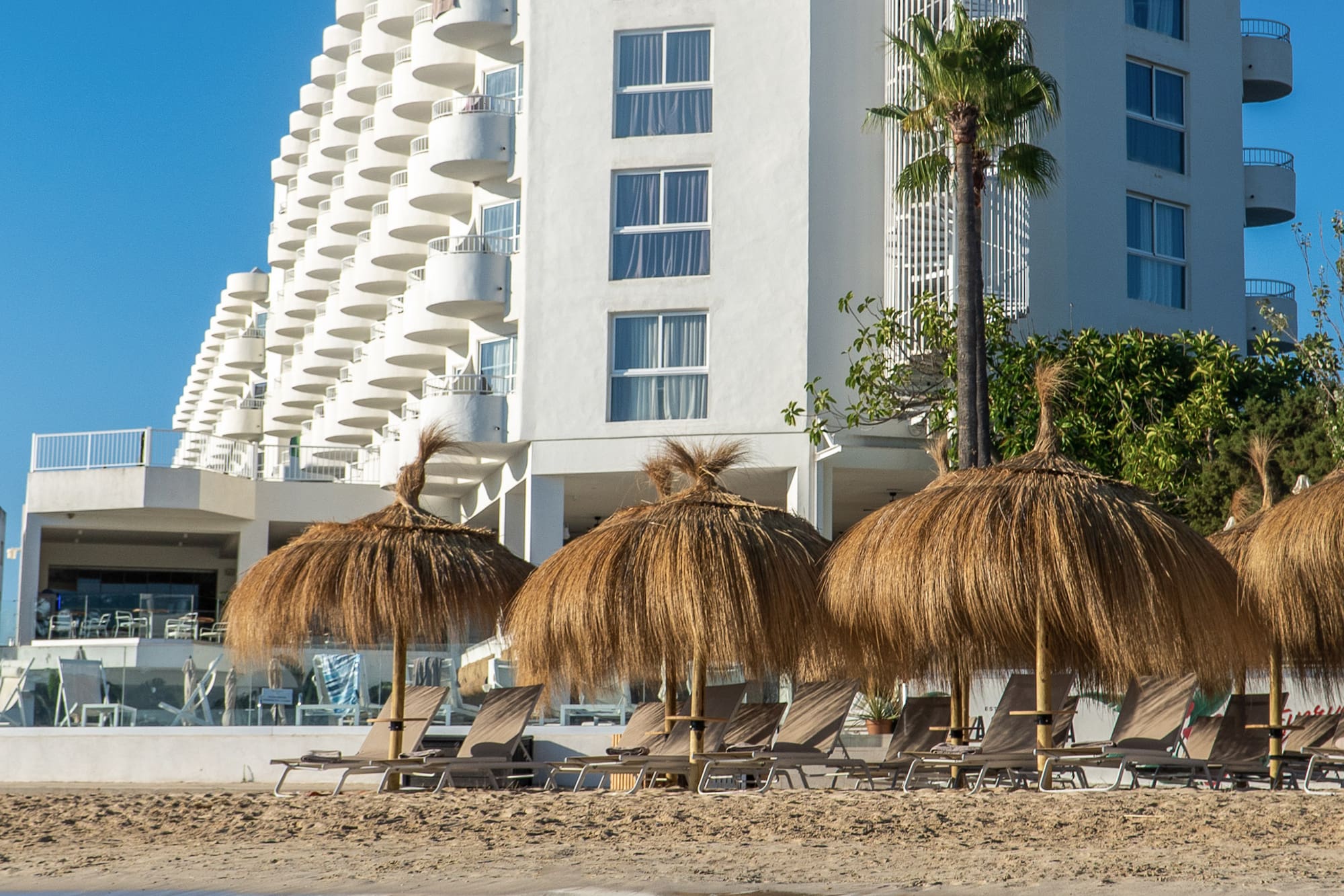 Waterfront INNSIDE hotel with beach umbrellas, lounge chairs, and clear blue sky.