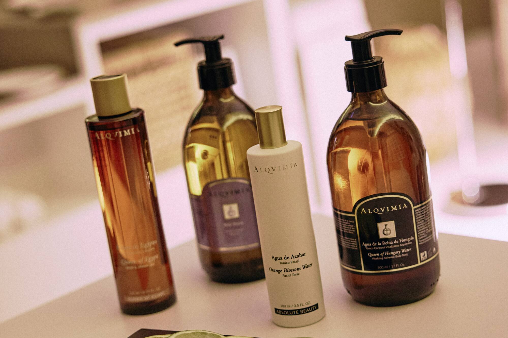 Four Alqvimia skincare bottles, including tonics, with lemon and lime slices.