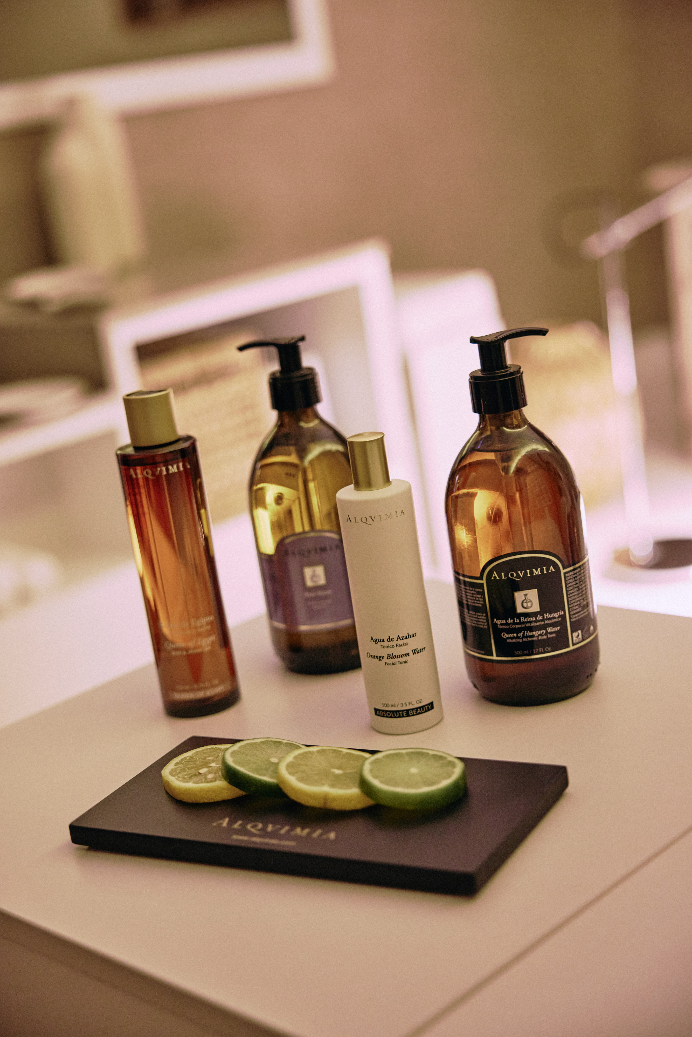 Four Alqvimia skincare bottles, including tonics, with lemon and lime slices.