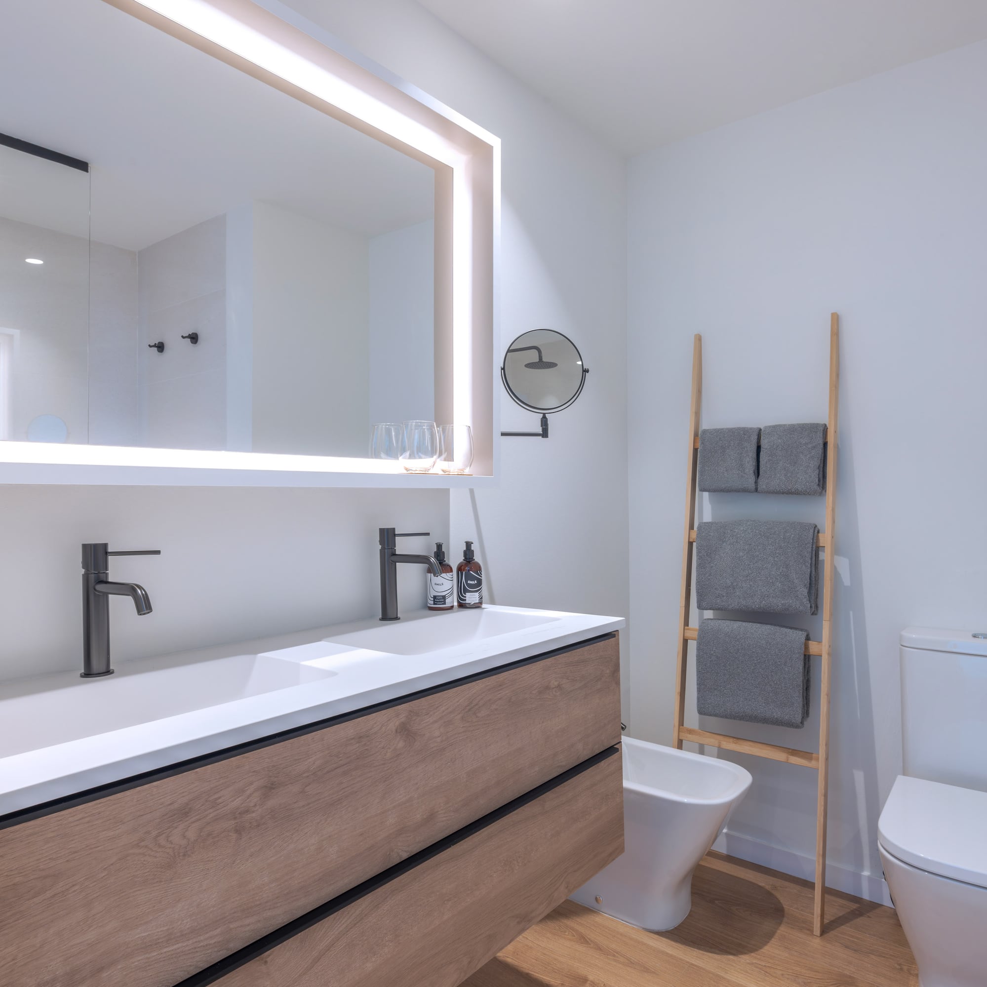 Baño moderno con mueble de madera, doble lavabo blanco y espejo iluminado.