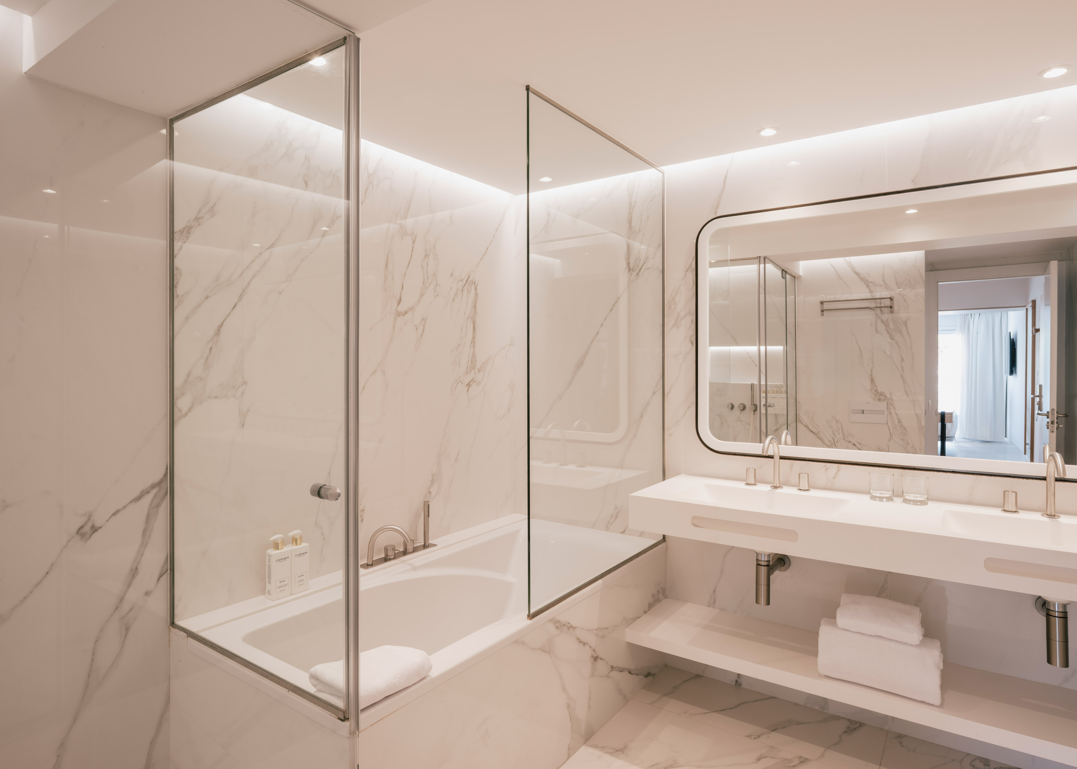 Luxurious marble bathroom with bathtub, glass partition, and double vanity.