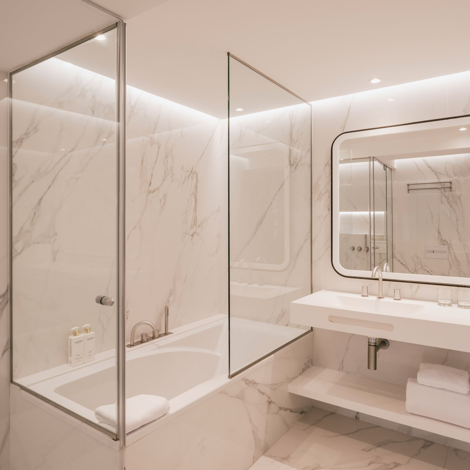 Luxurious marble bathroom with bathtub, glass partition, and double vanity.