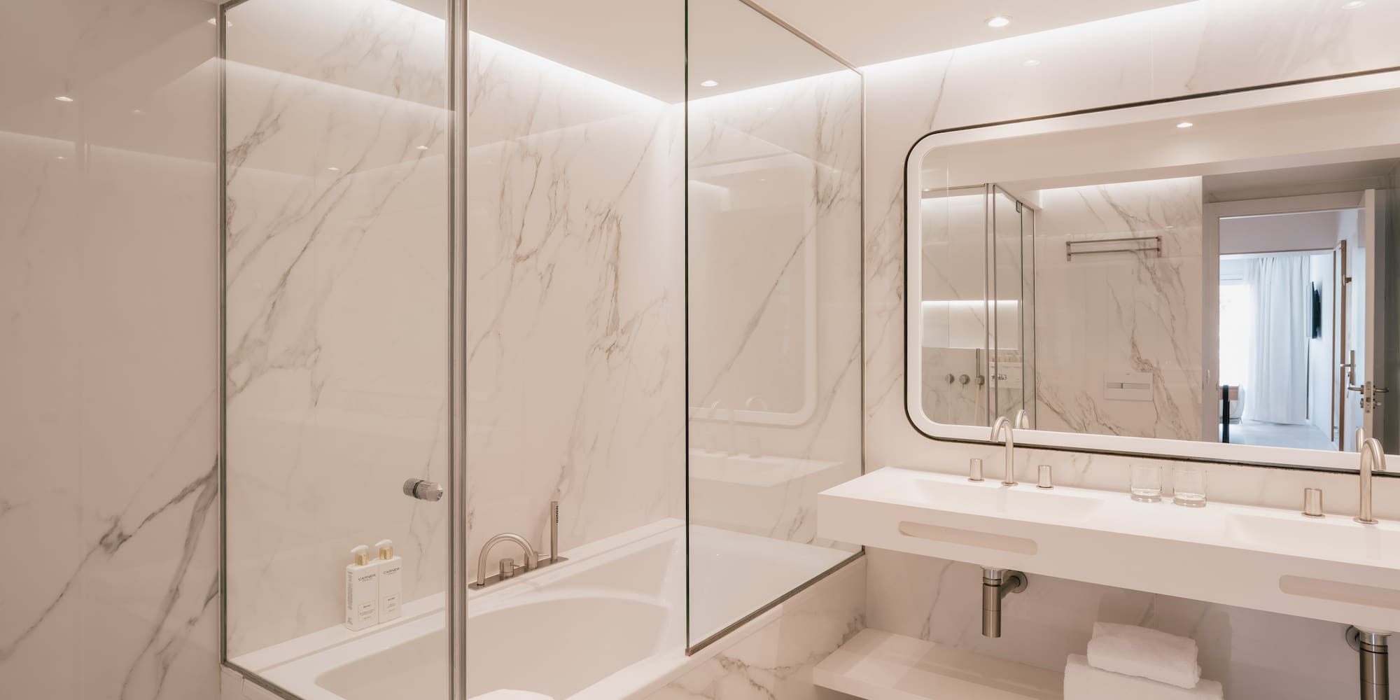 Luxurious marble bathroom with bathtub, glass partition, and double vanity.
