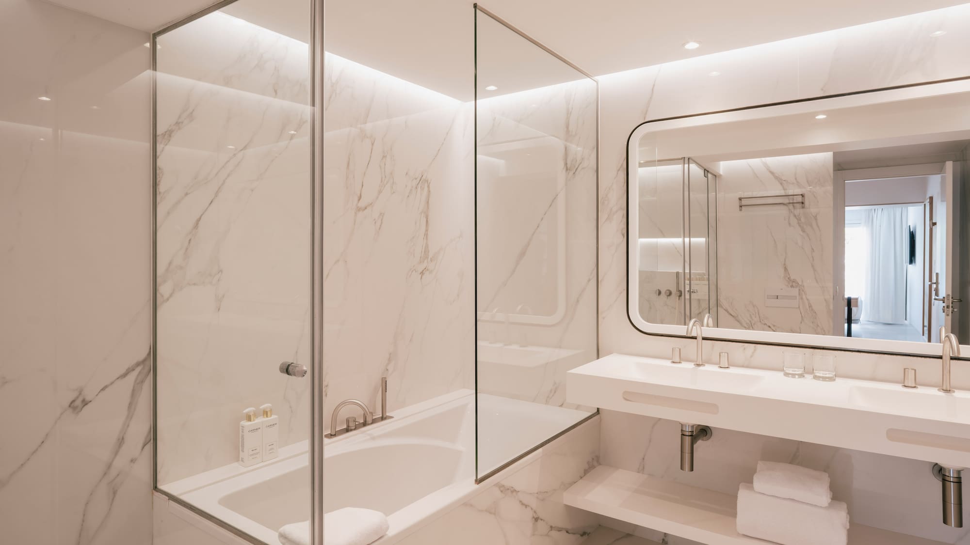 Luxurious marble bathroom with bathtub, glass partition, and double vanity.