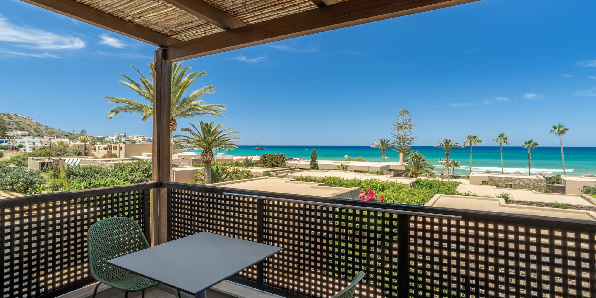 Scenic balcony with turquoise sea view, palm trees, and coastal resort.
