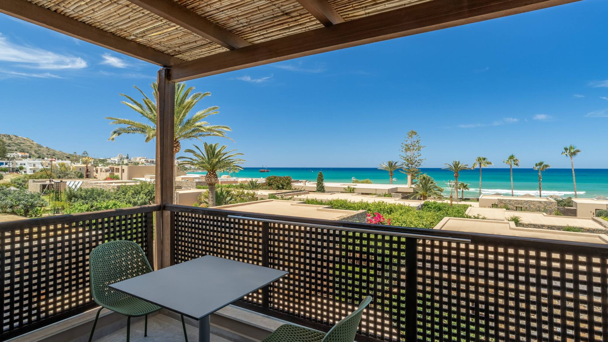 Scenic balcony with turquoise sea view, palm trees, and coastal resort.