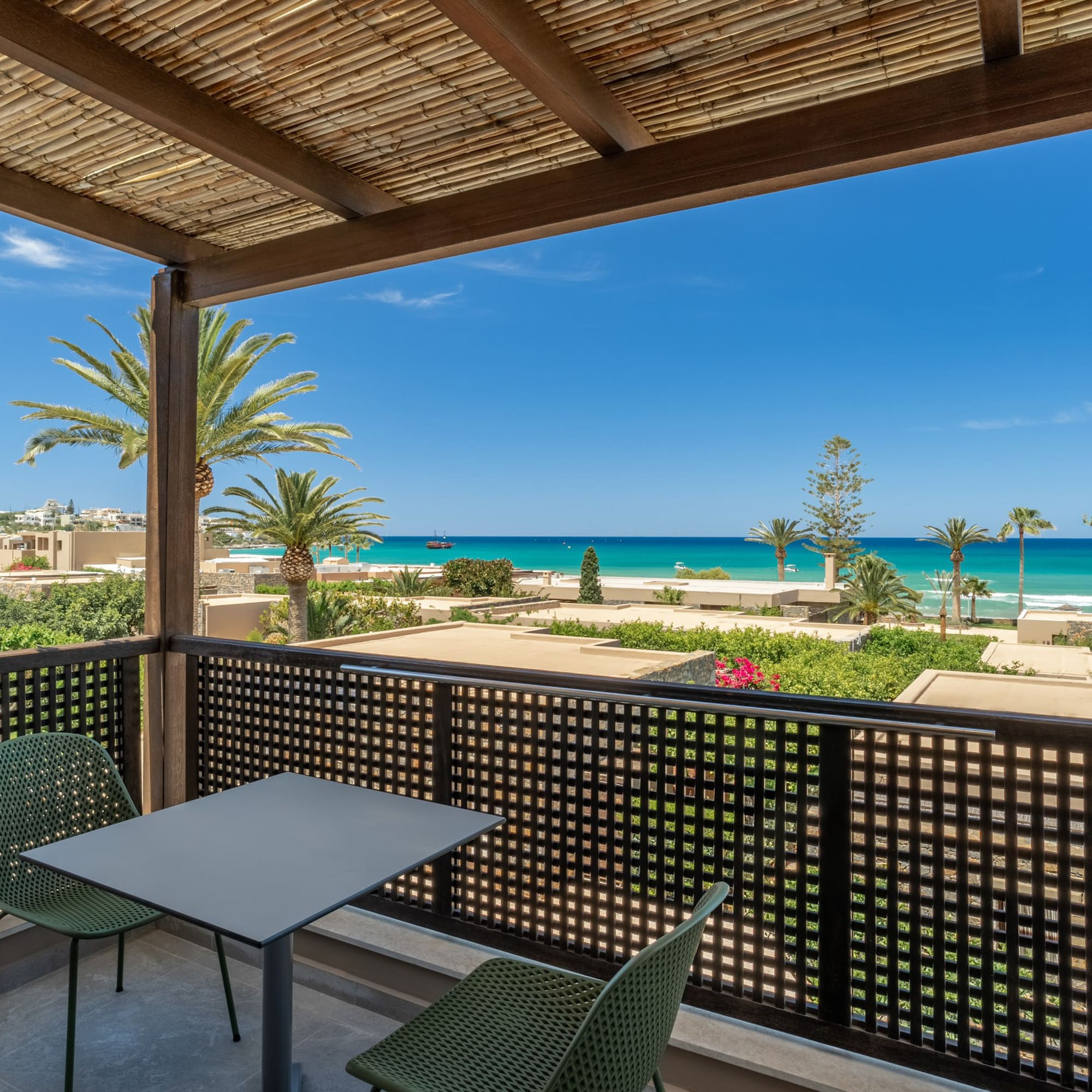 Scenic balcony with turquoise sea view, palm trees, and coastal resort.