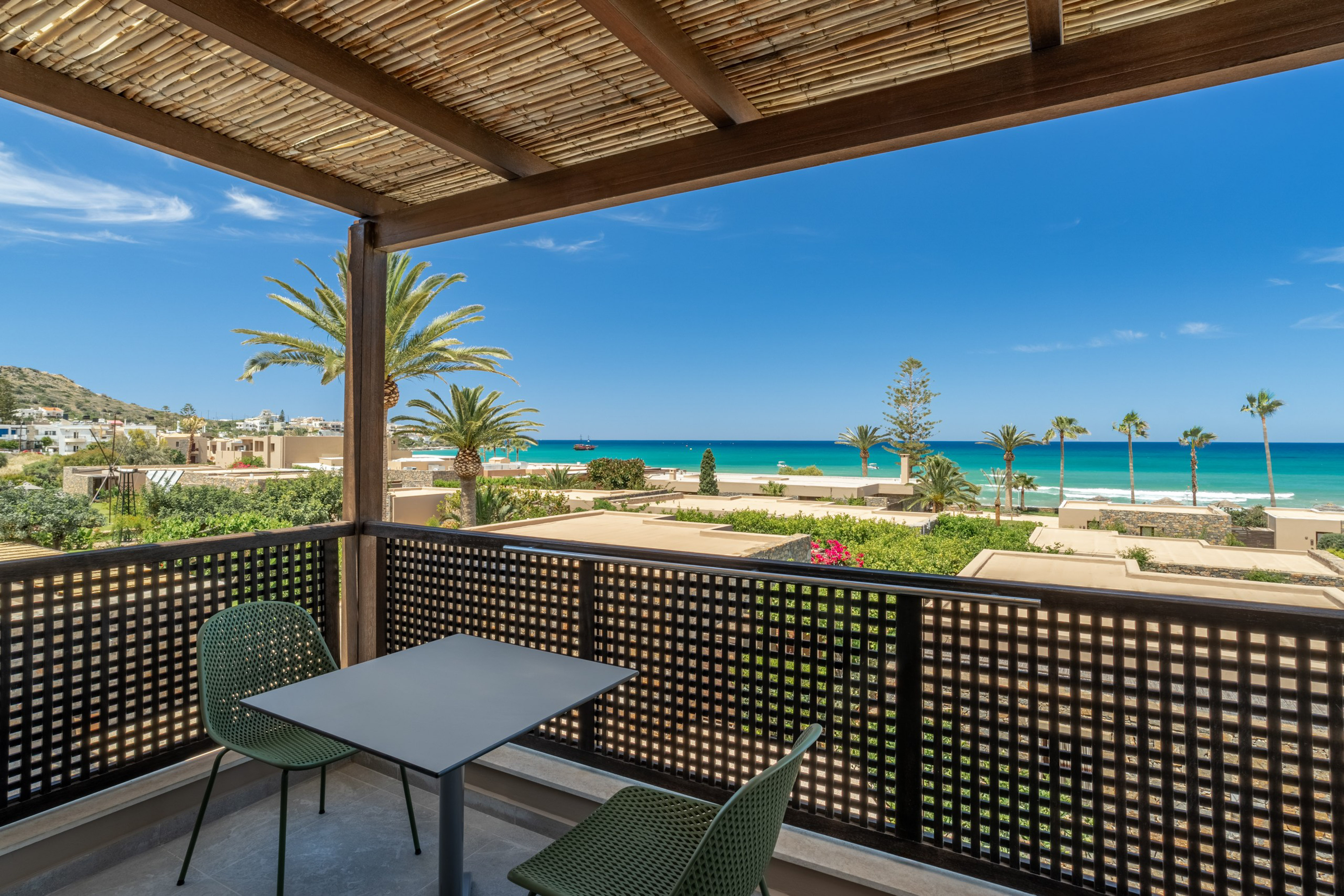 Scenic balcony with turquoise sea view, palm trees, and coastal resort.