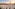 White stupas surround golden pagoda at a Thai temple with mountains, sunset.