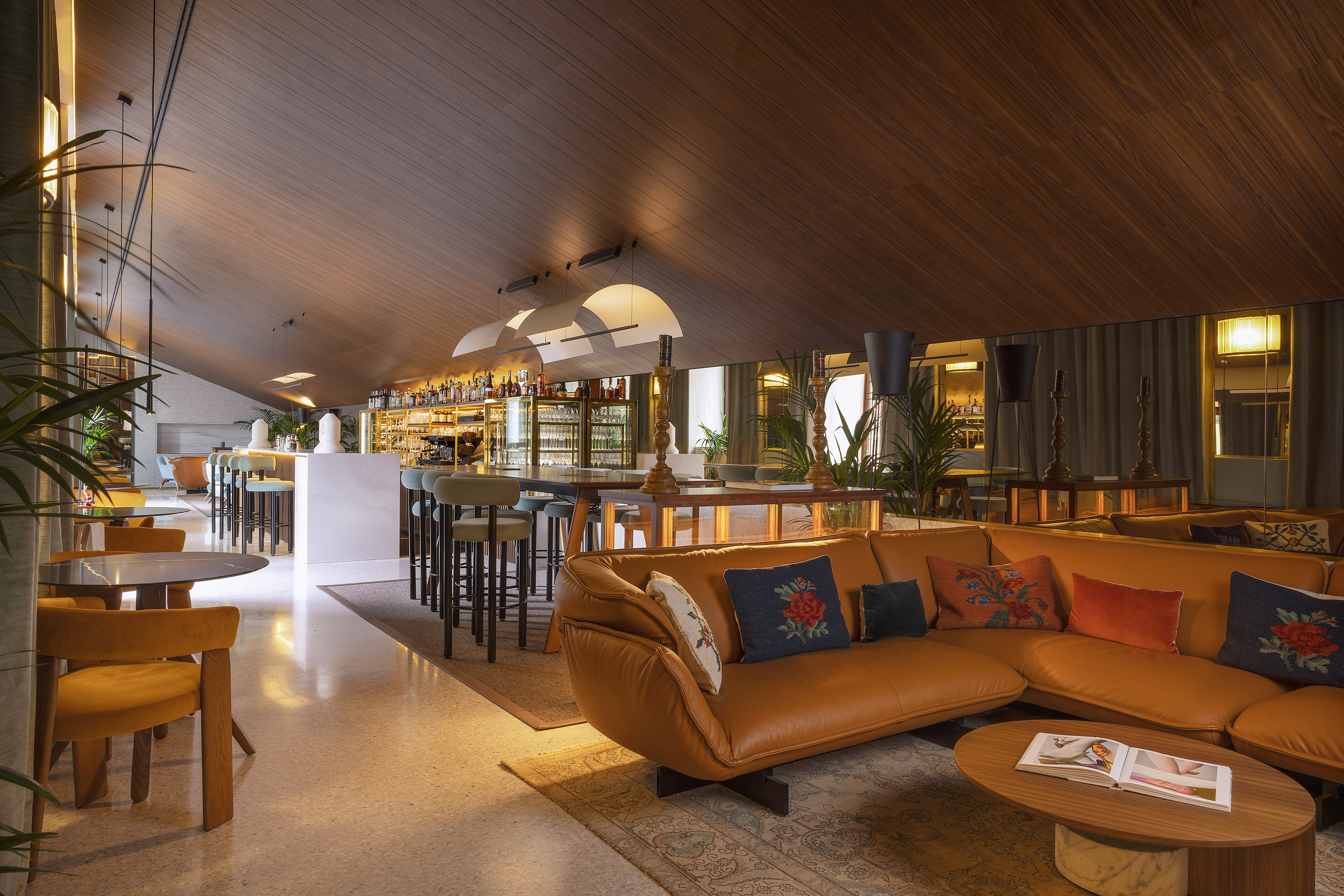 Modern lounge bar with wooden ceiling, tan leather sofa, and white bar counter.