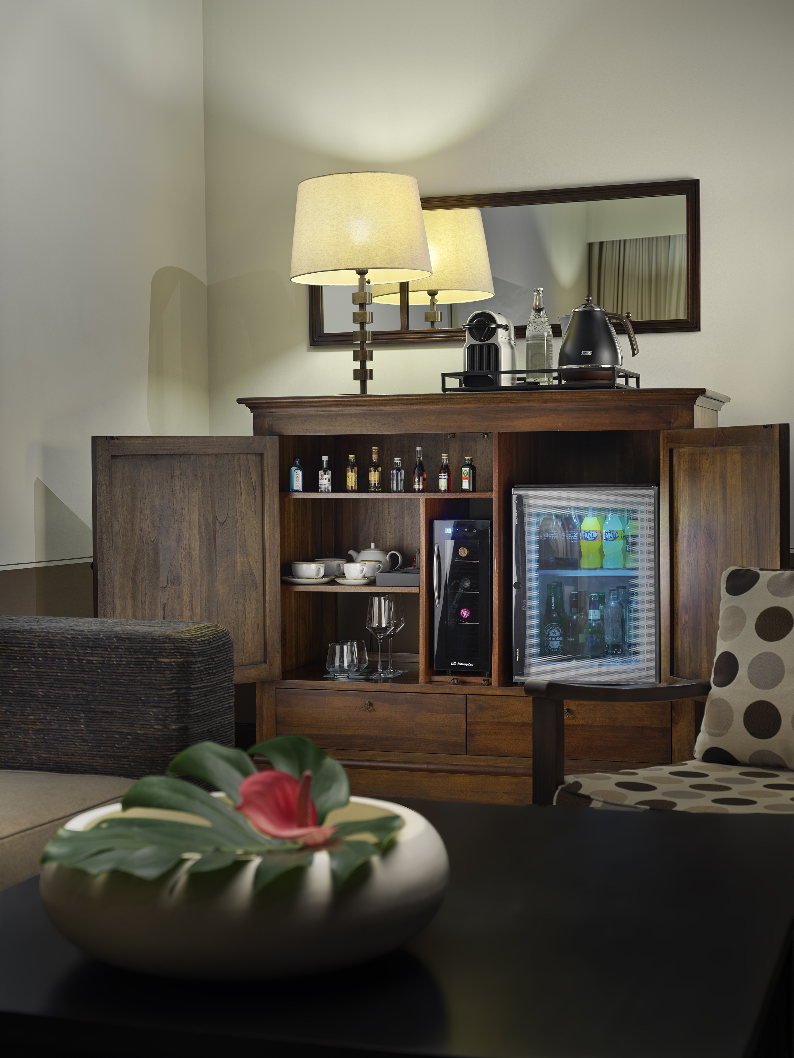 Hotel room minibar cabinet with drinks, coffee maker, wine cooler, and kettle.