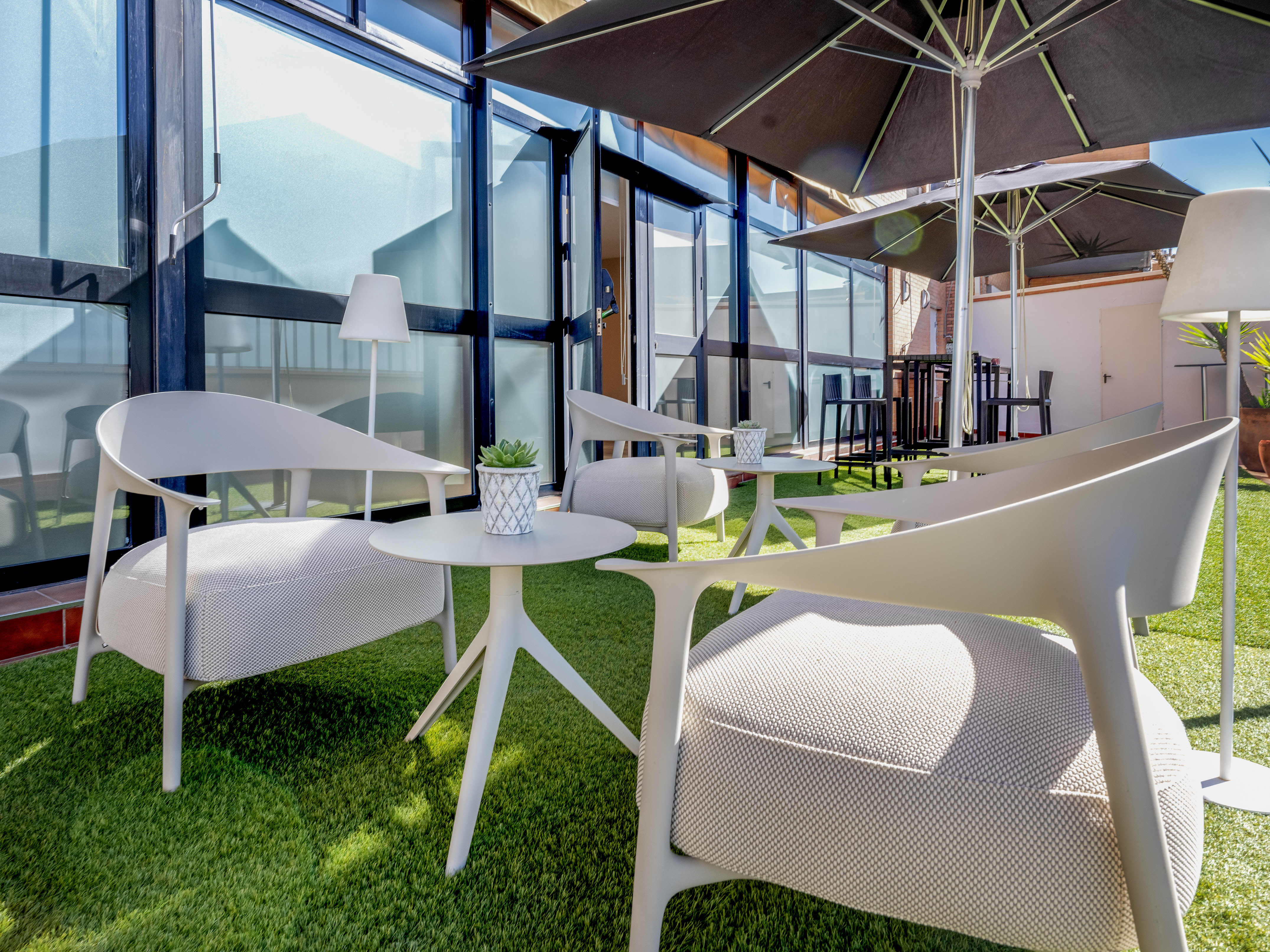 Outdoor terrace with modern seating, black umbrellas, artificial green grass.