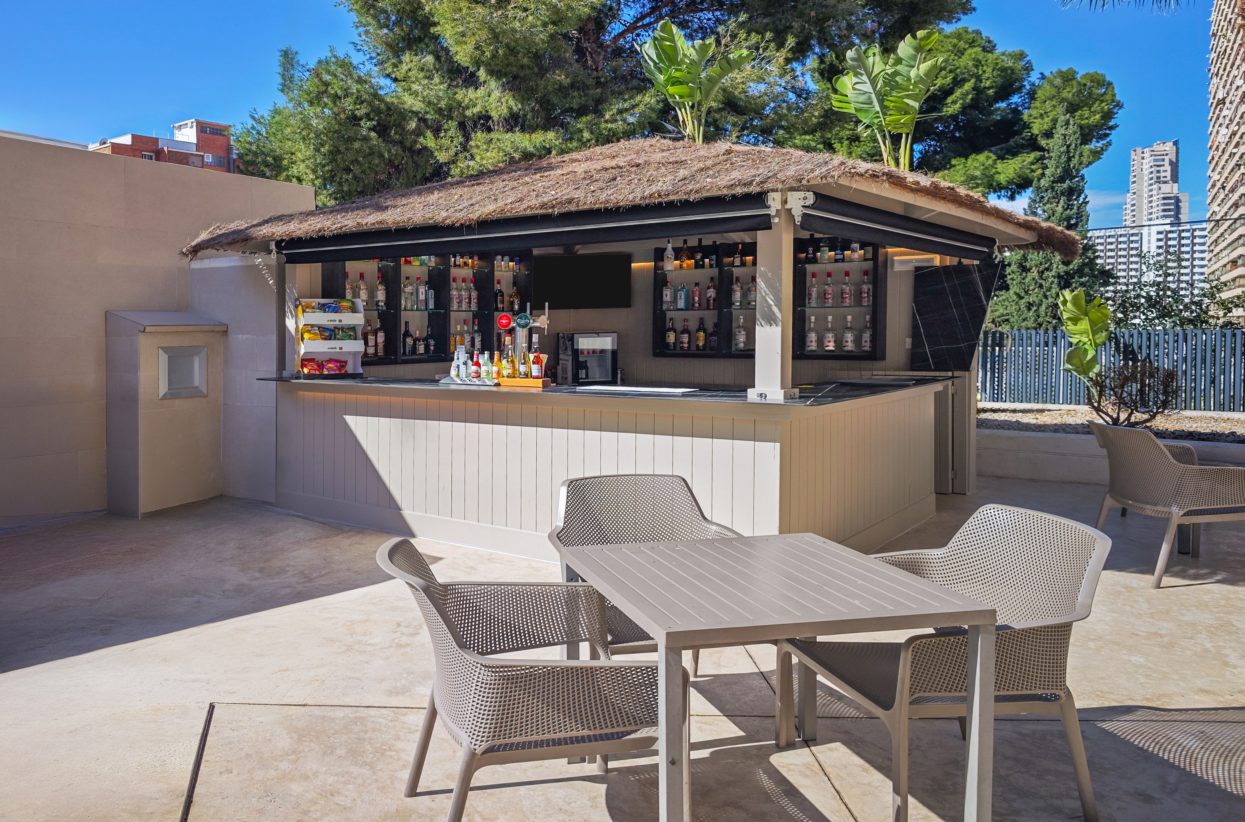 Sunny outdoor bar with thatched roof, liquor, and patio seating.