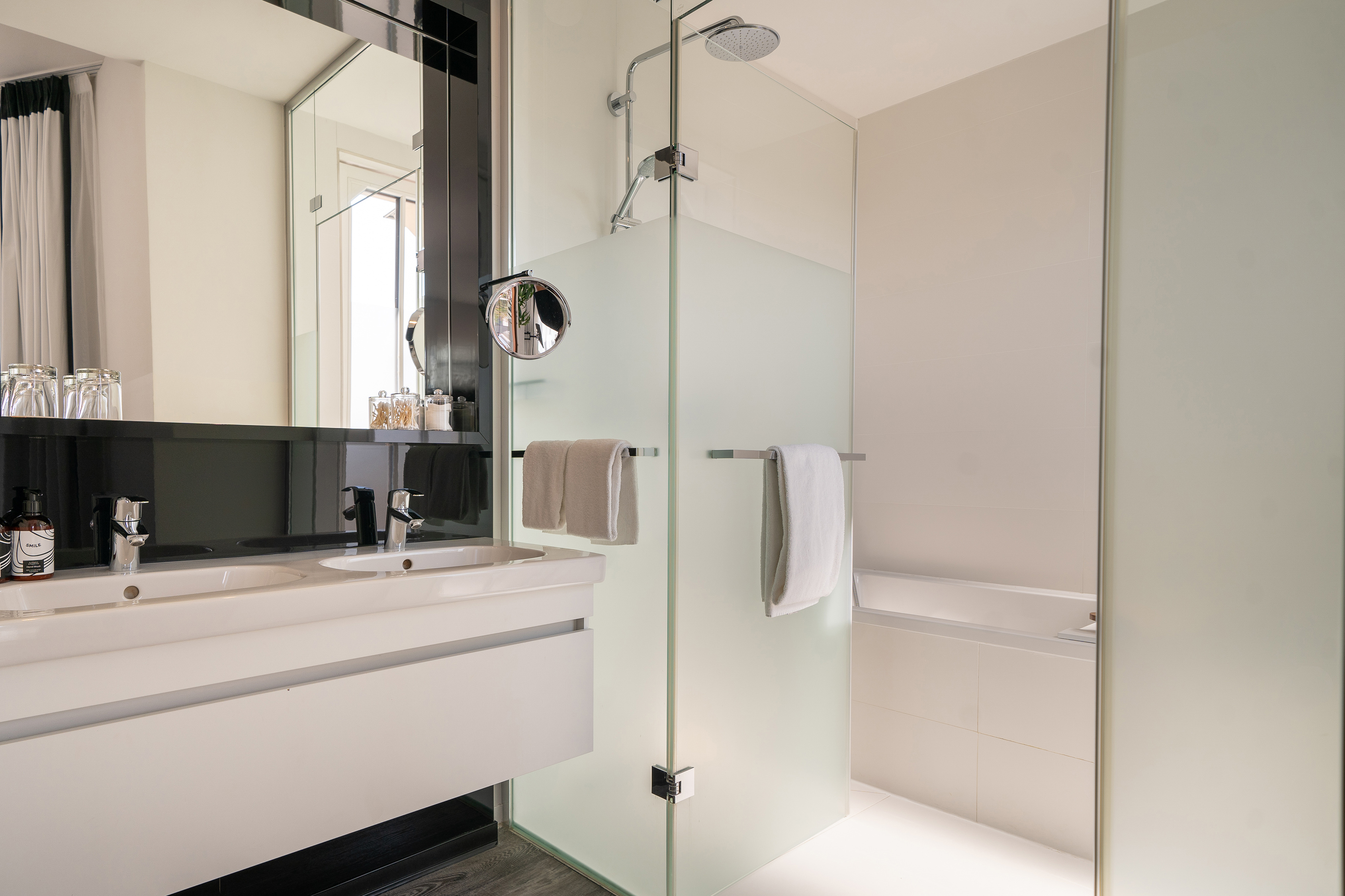 Modern hotel bathroom with double vanity, frosted glass shower, and bathtub.
