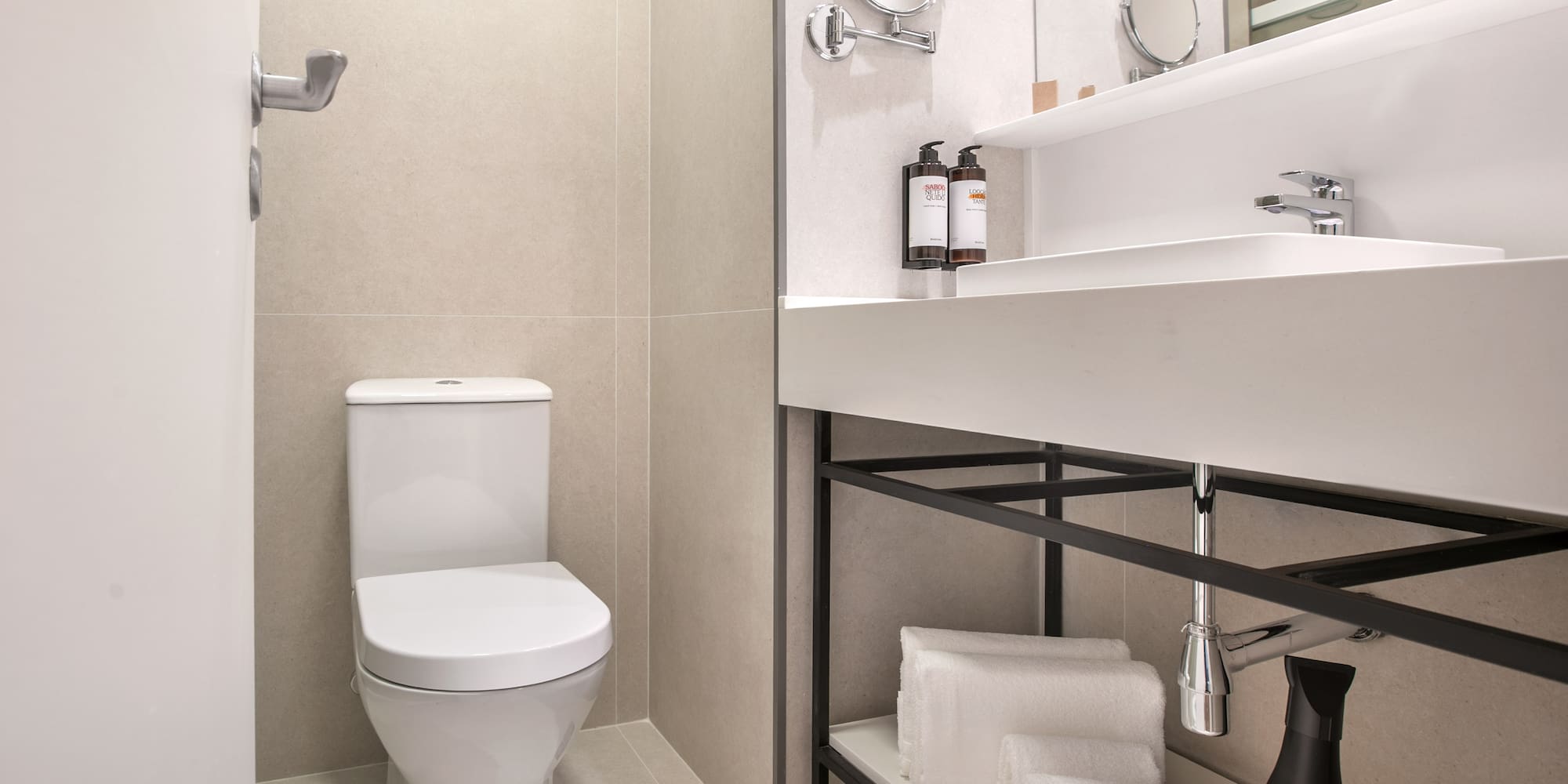 Modern hotel bathroom with white toilet, sink, mirror, and folded towels.