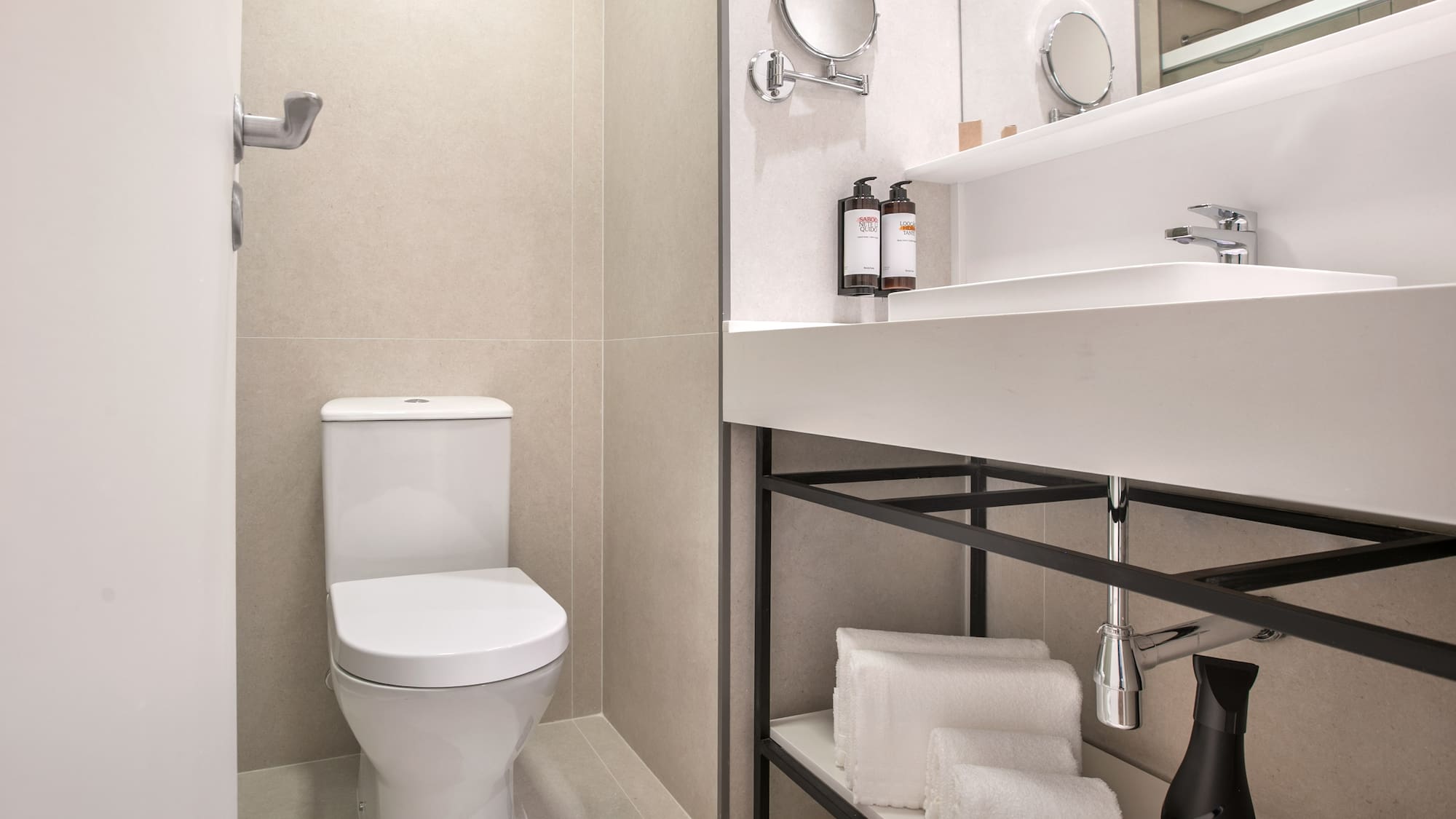 Modern hotel bathroom with white toilet, sink, mirror, and folded towels.