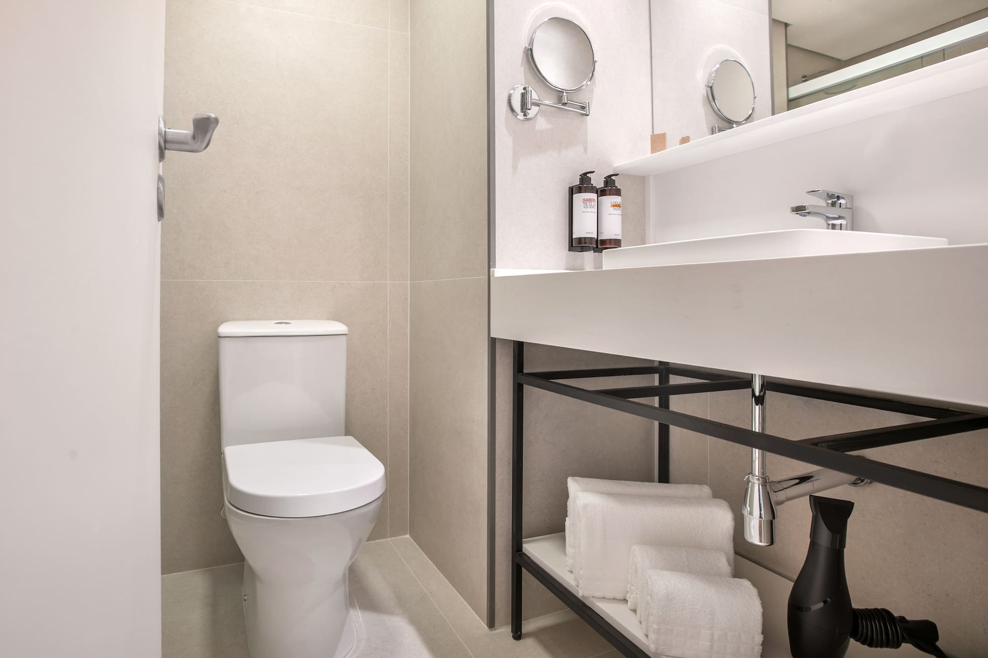 Modern hotel bathroom with white toilet, sink, mirror, and folded towels.