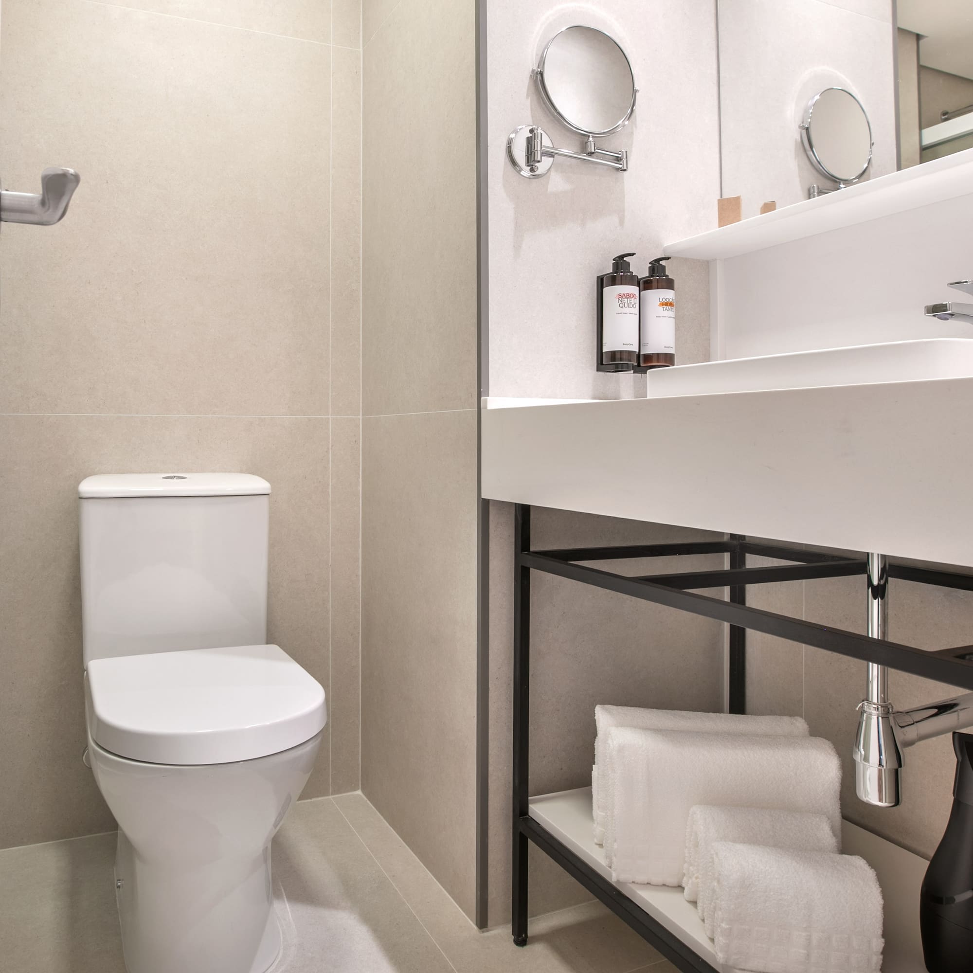 Modern hotel bathroom with white toilet, sink, mirror, and folded towels.