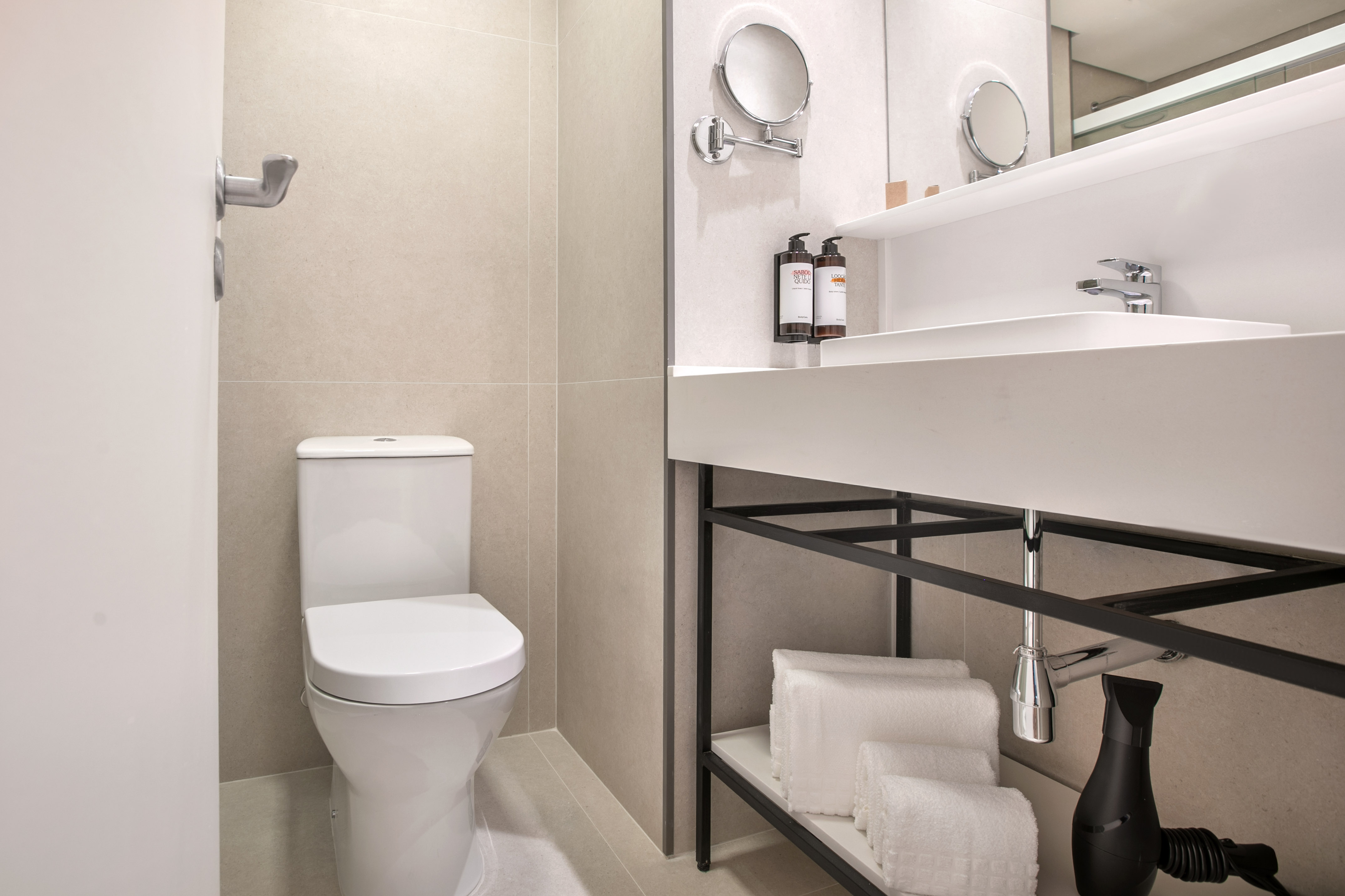 Modern hotel bathroom with white toilet, sink, mirror, and folded towels.