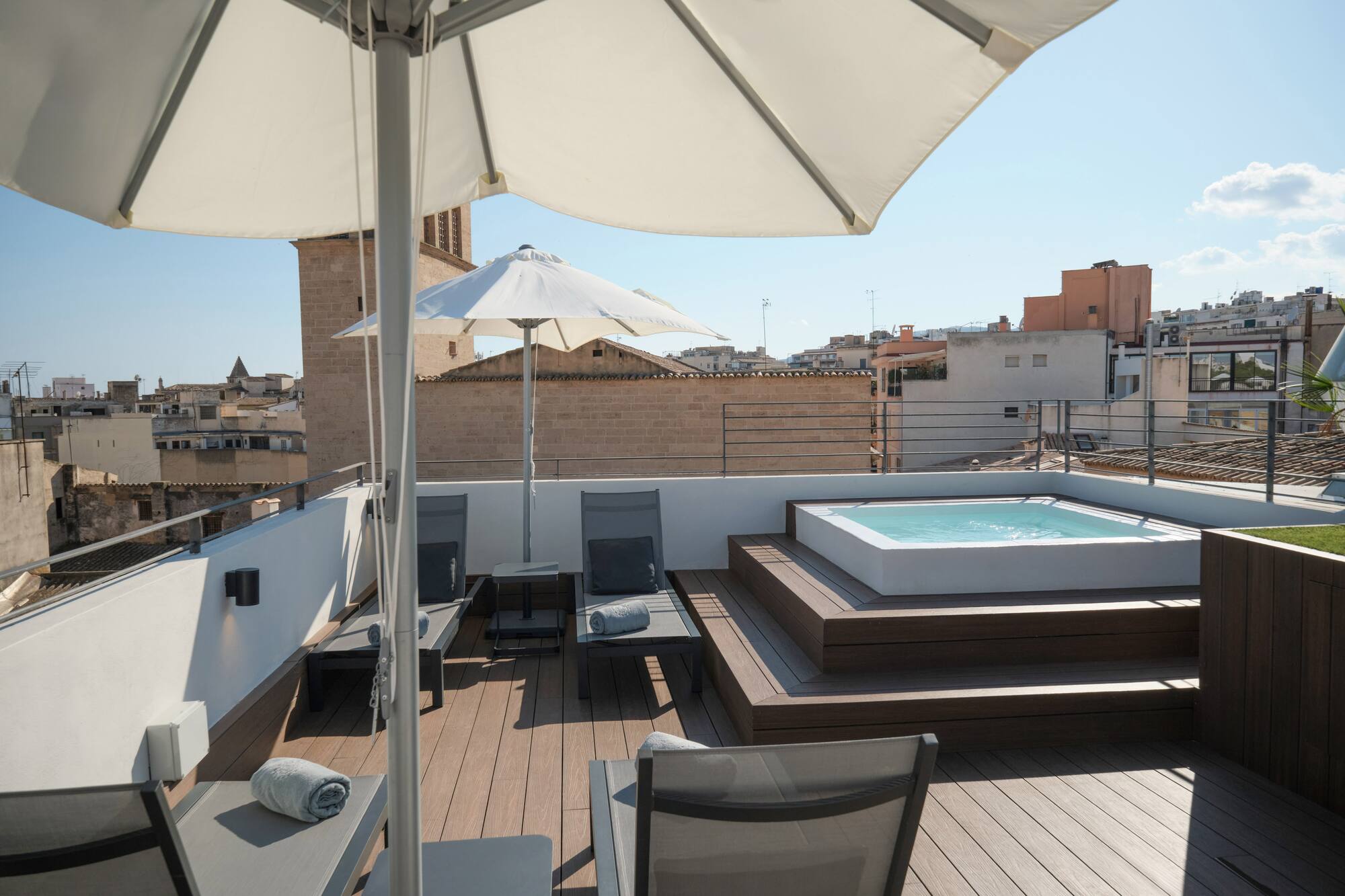 Rooftop terrace with jacuzzi, lounge chairs, umbrellas, and city view.