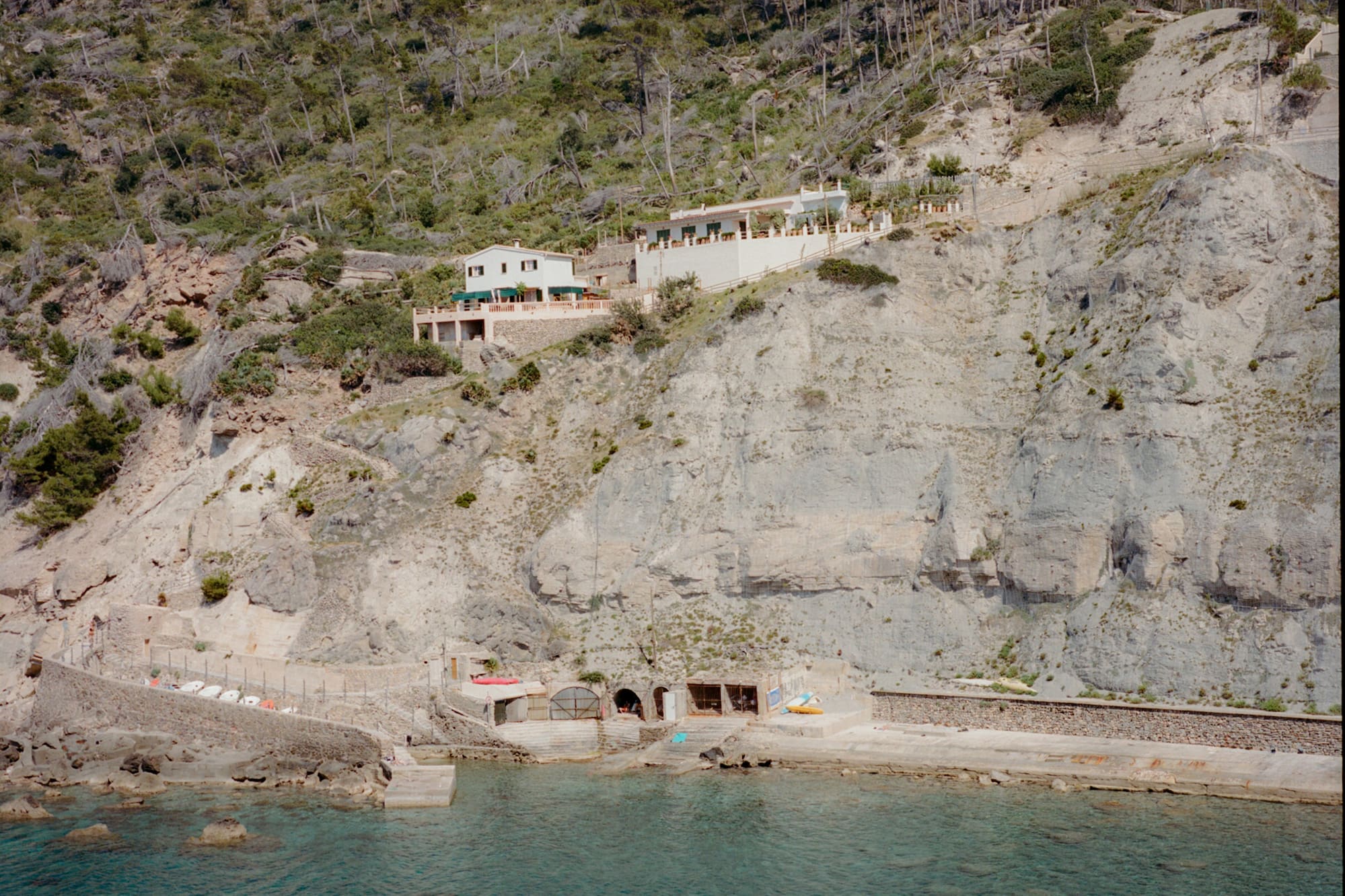 Cala con casas en acantilado boscoso y aguas turquesas, Mallorca.