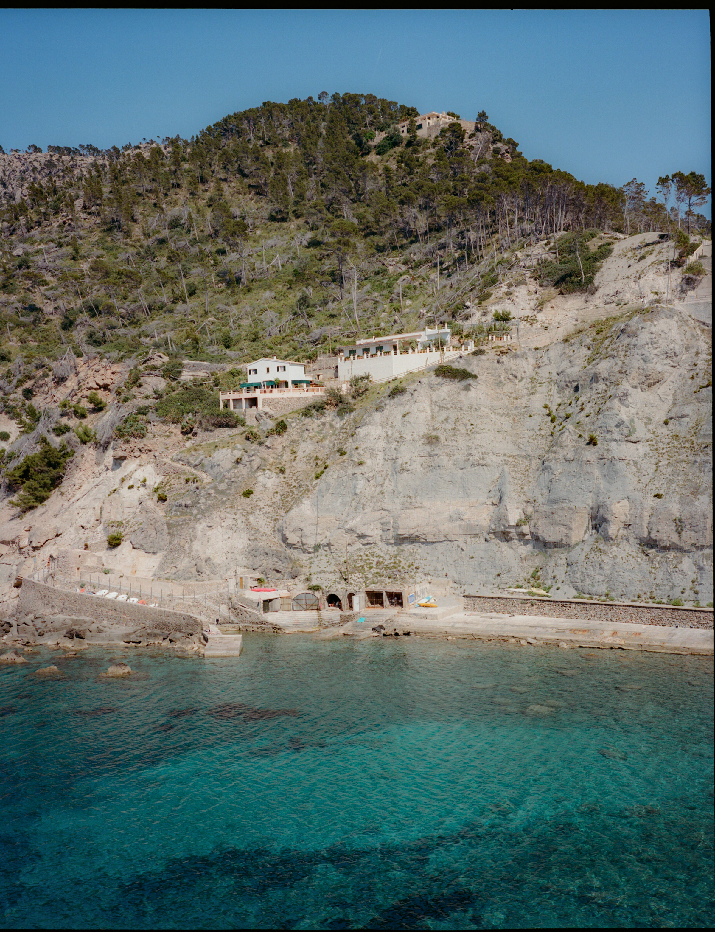 Cala con casas en acantilado boscoso y aguas turquesas, Mallorca.
