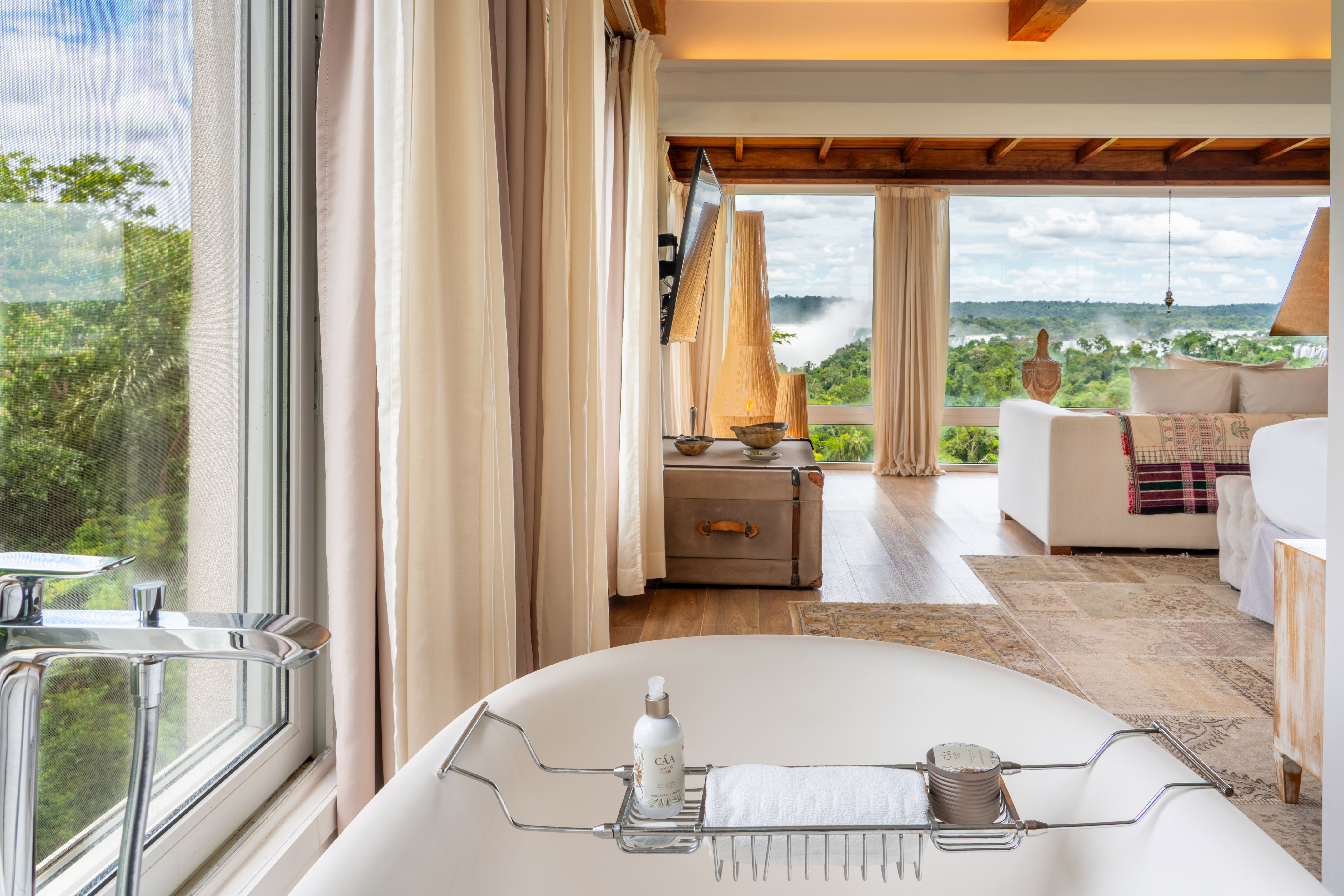 Bathtub in luxury suite with panoramic window view of rainforest waterfalls.