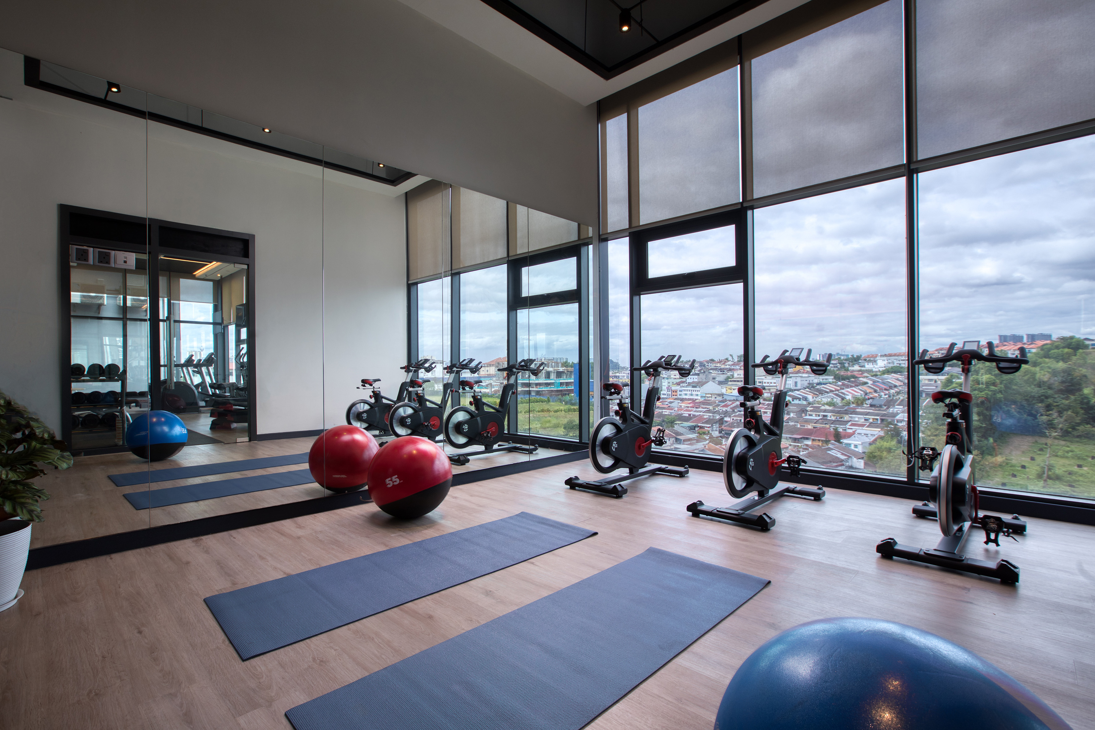 Modern gym with spinning bikes, yoga mats, exercise balls, city view.