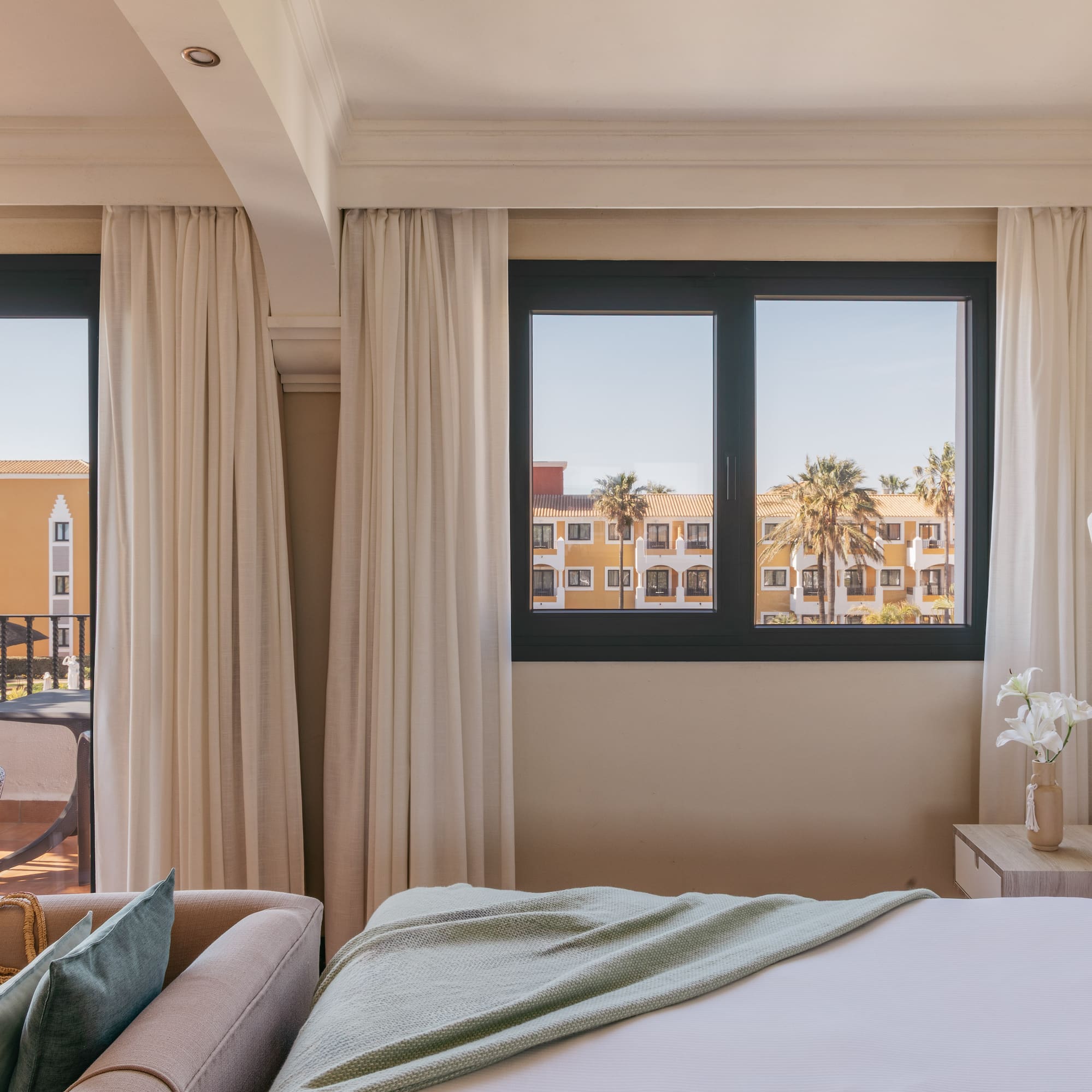 Resort hotel room with ocean view, balcony, palm trees, comfortable bed.