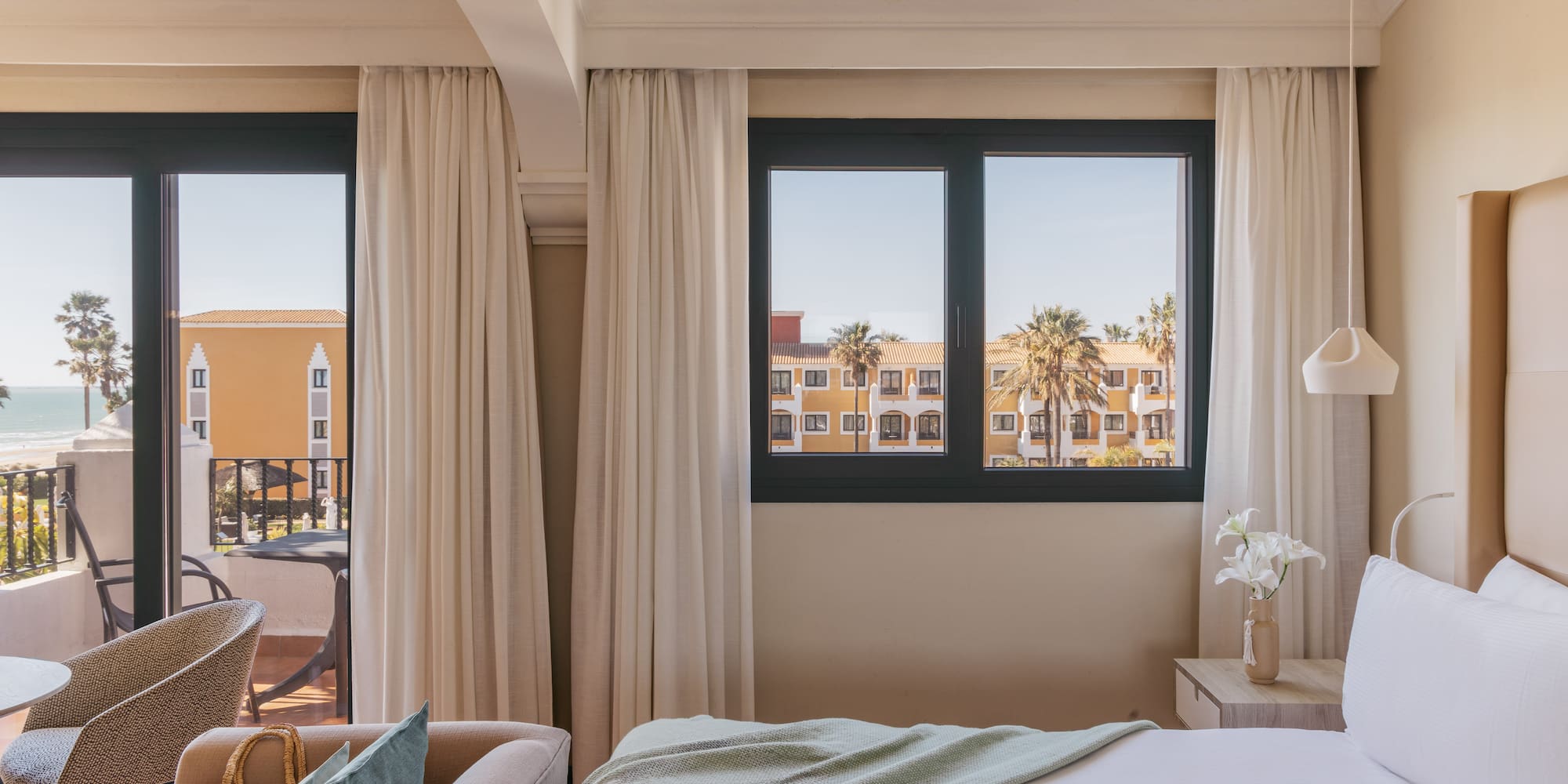 Resort hotel room with ocean view, balcony, palm trees, comfortable bed.