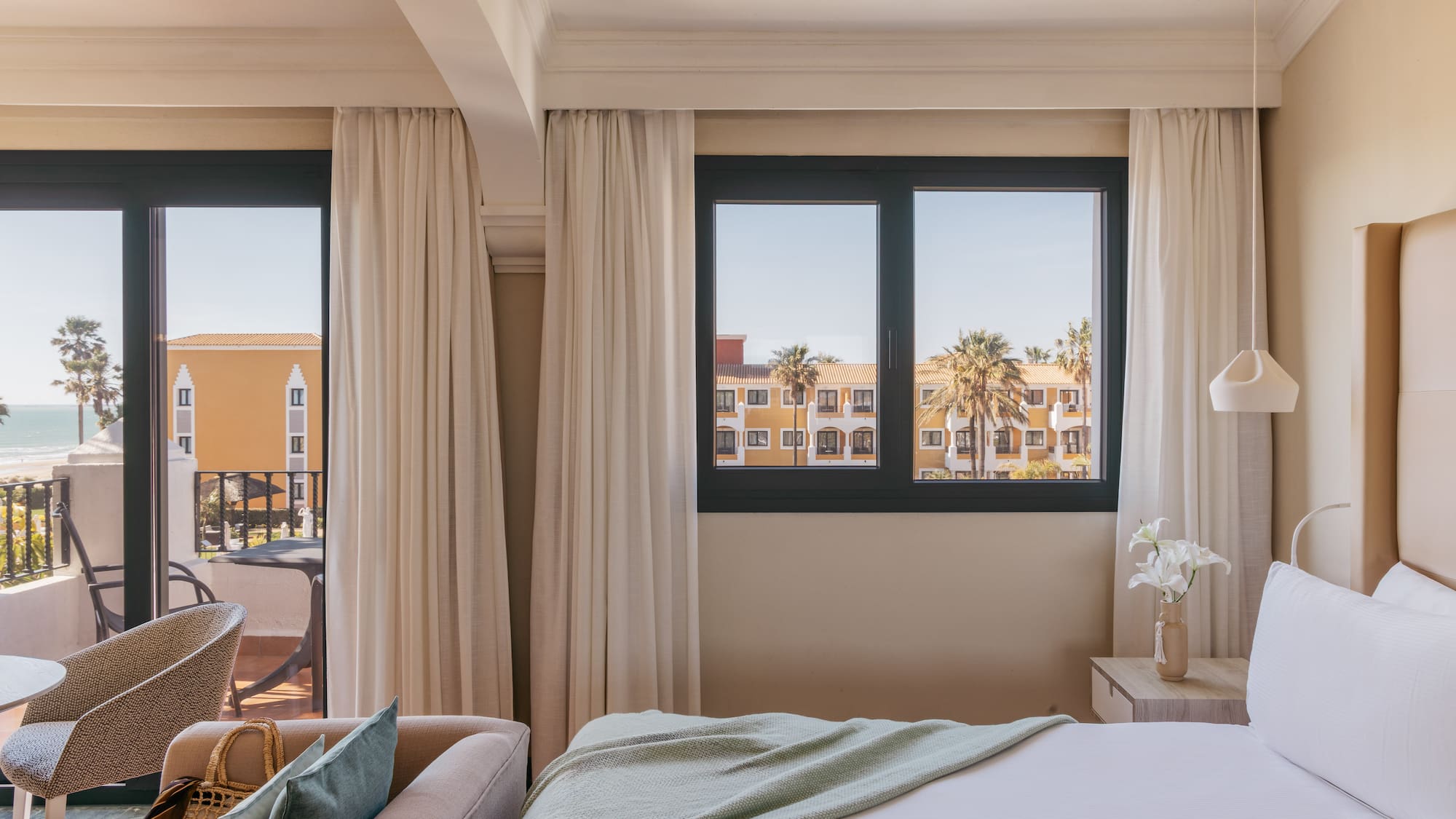 Resort hotel room with ocean view, balcony, palm trees, comfortable bed.