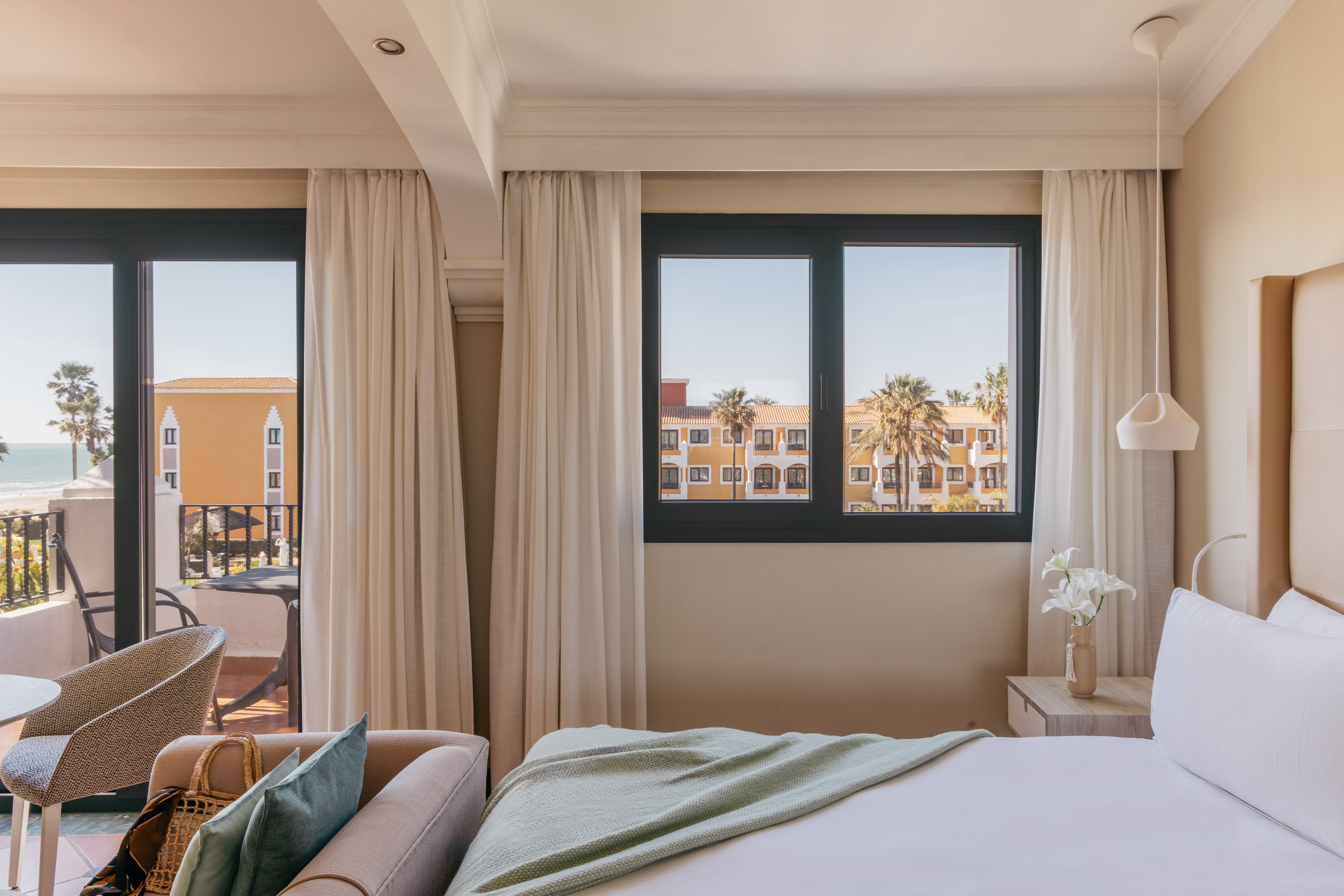 Resort hotel room with ocean view, balcony, palm trees, comfortable bed.