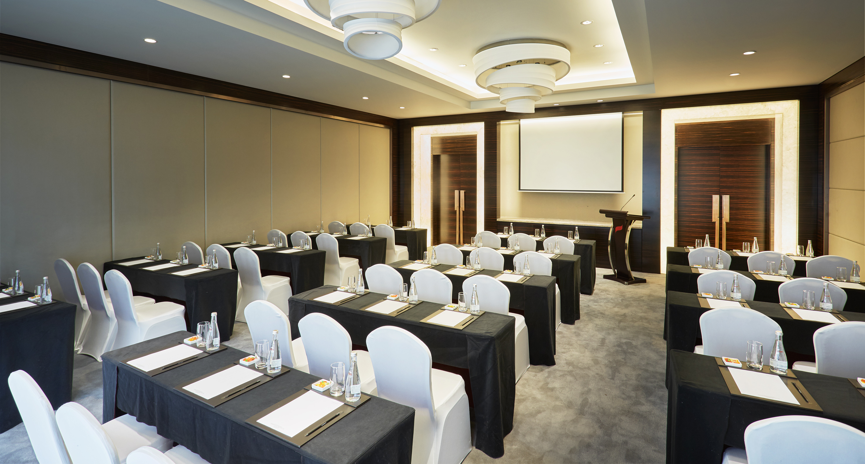 Modern conference room with classroom setup, screen, and lectern.
